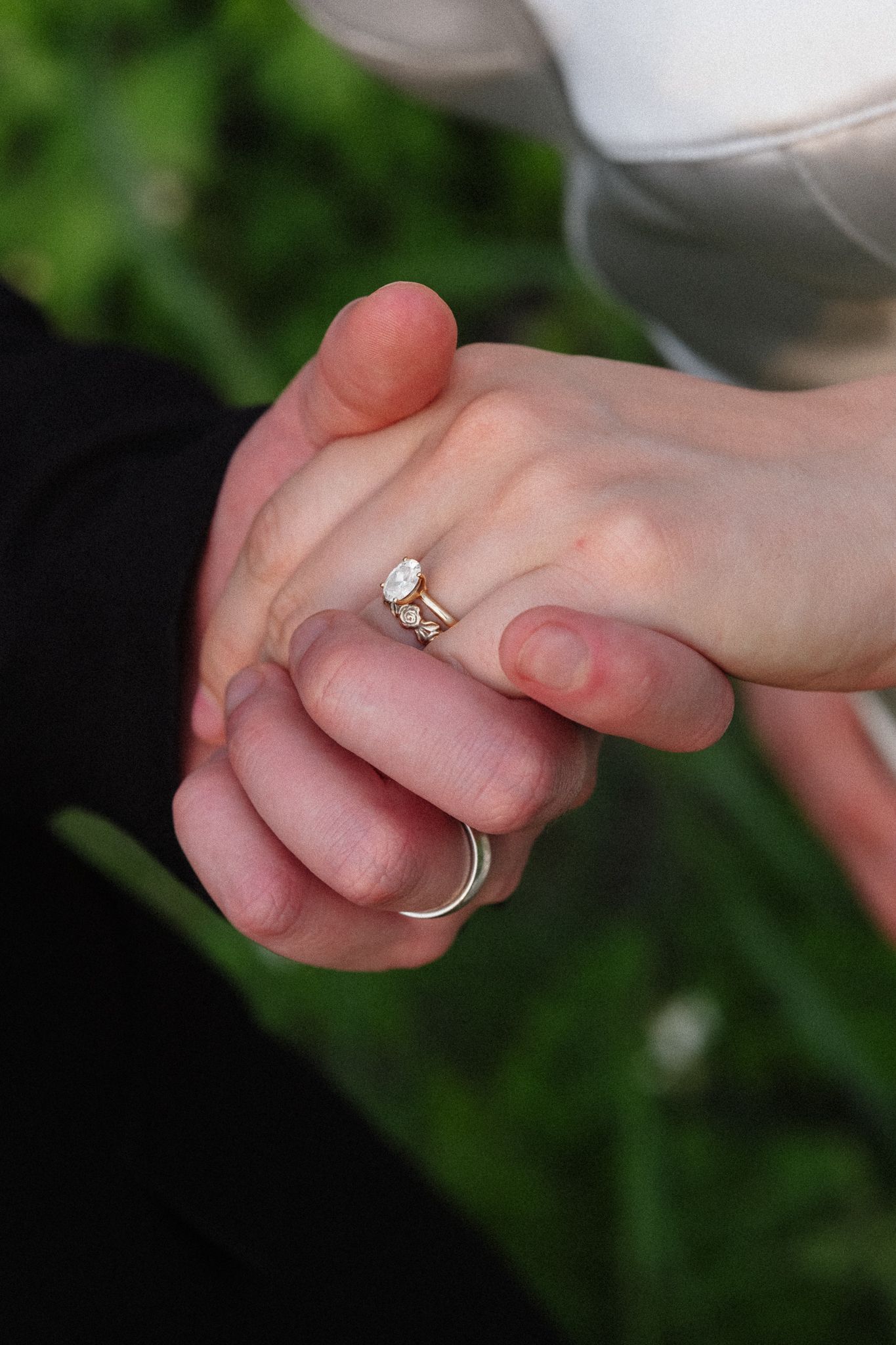 Close-up of two hands holding, showcasing a diamond engagement ring and wedding band on the woman's finger.