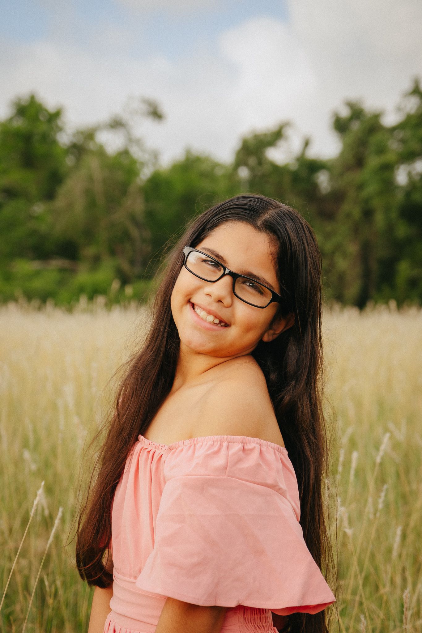 A series of warm portraits showing someone in a pink off-shoulder top posing cheerfully in a sunlit meadow.