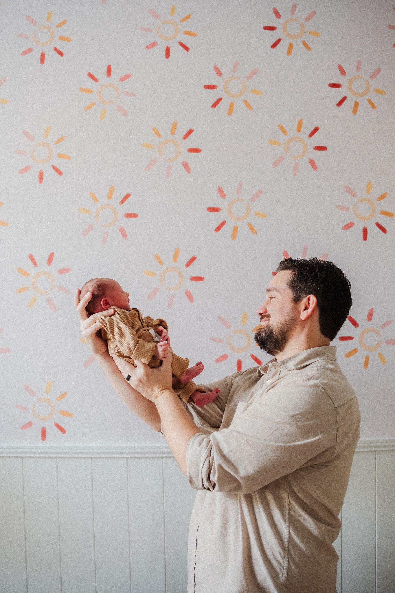A sequence showing a person in beige clothing lifting and holding a baby against a wall with orange starburst patterns.