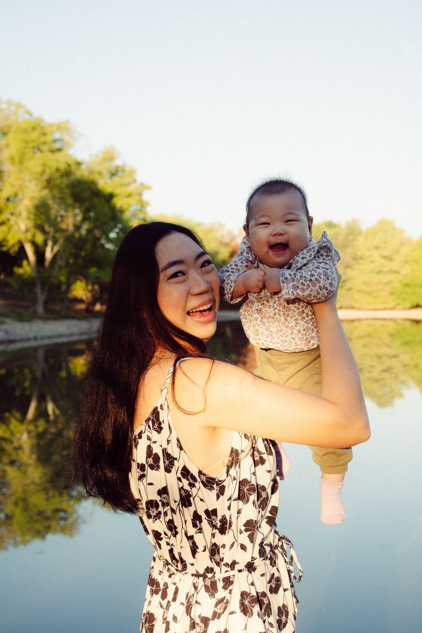 Mother and baby share joyful moments by a serene lake during golden hour.