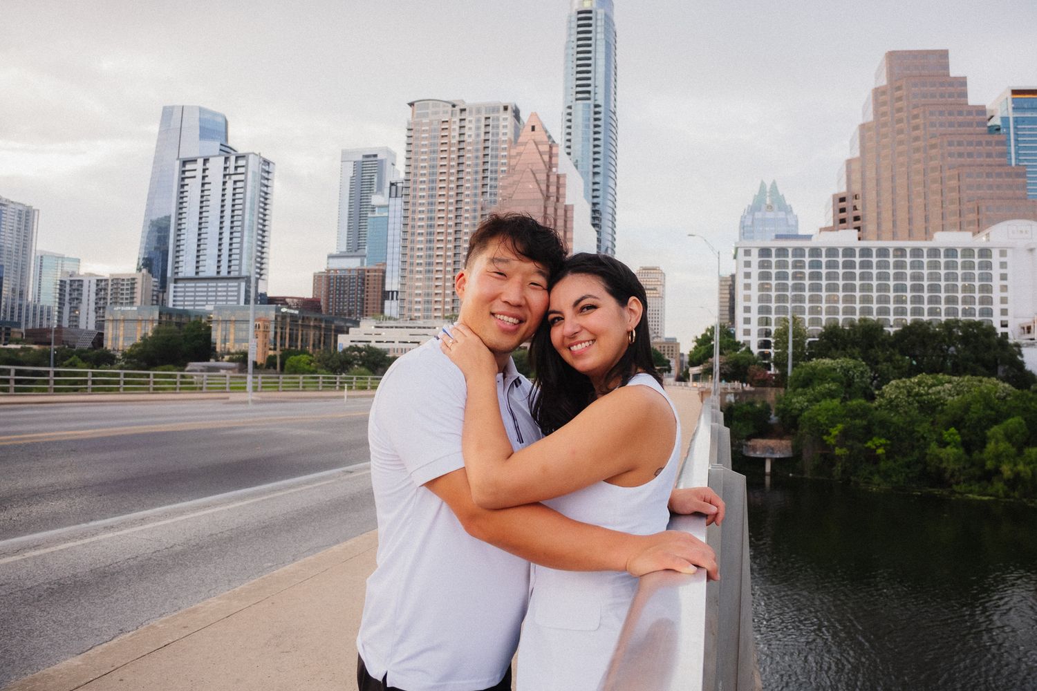 Couple embracing on a bridge with the Austin, Texas skyline and river in the background.