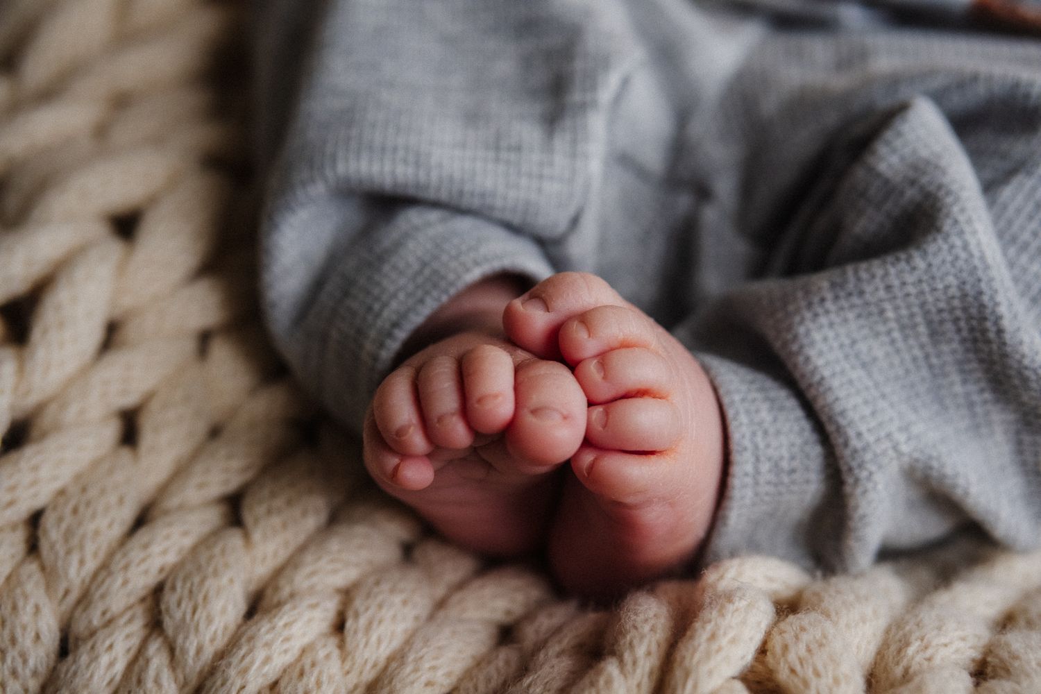 Close-up view of tiny baby feet and toes against a cozy knitted blanket background.