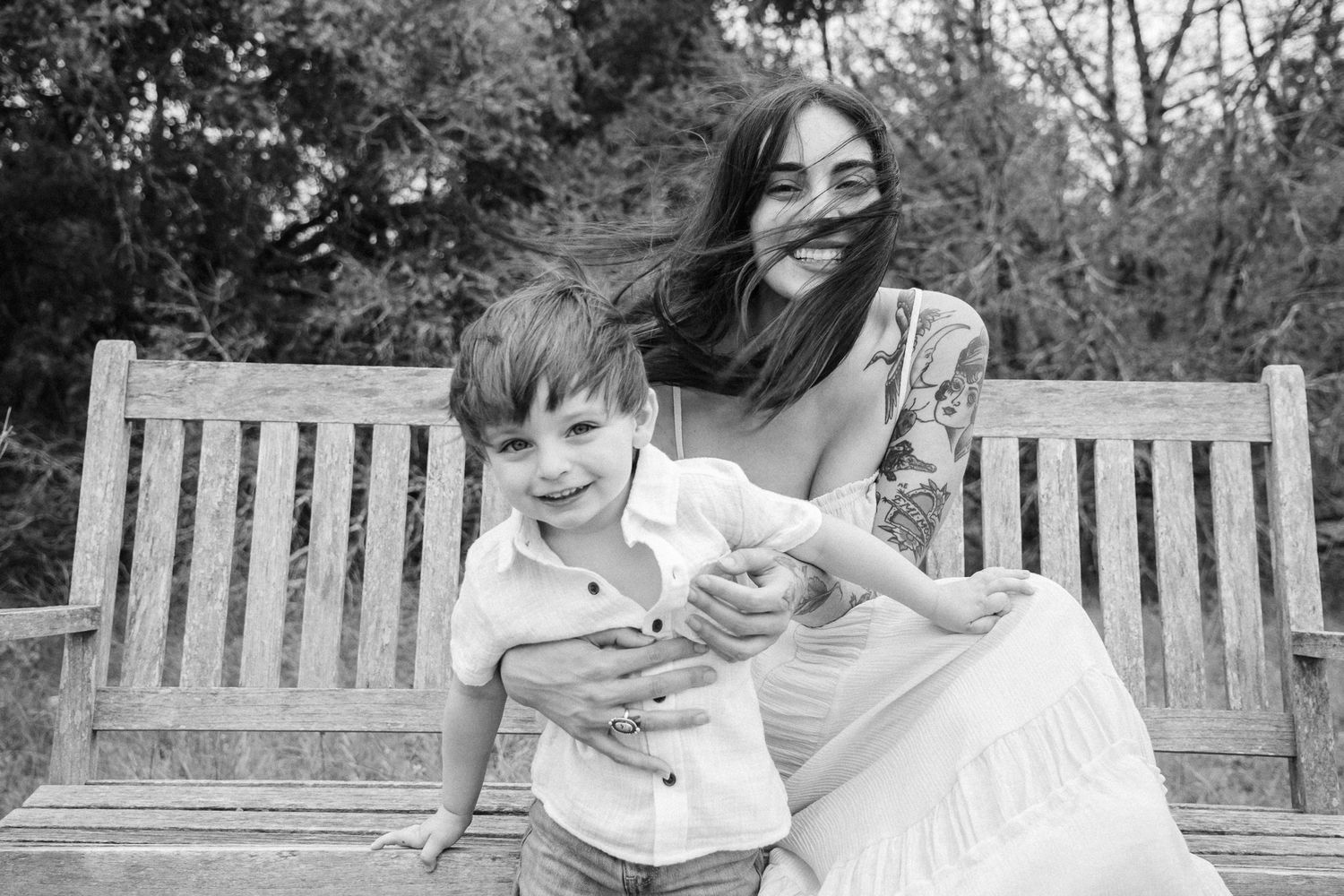 Black and white photo of a parent and child laughing together while sitting outdoors on a wooden bench.
