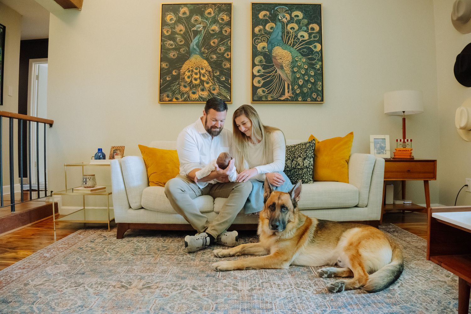 Mother and father holding their newborn on their couch while sitting next their dog.