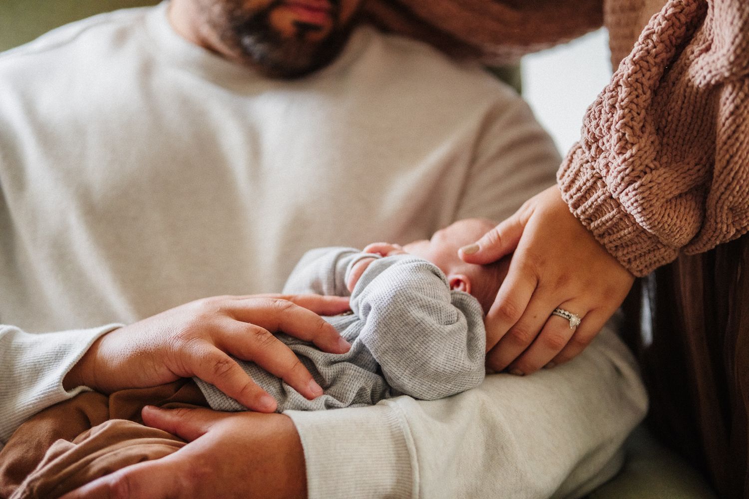 Close-up of hands tenderly holding baby against white background.