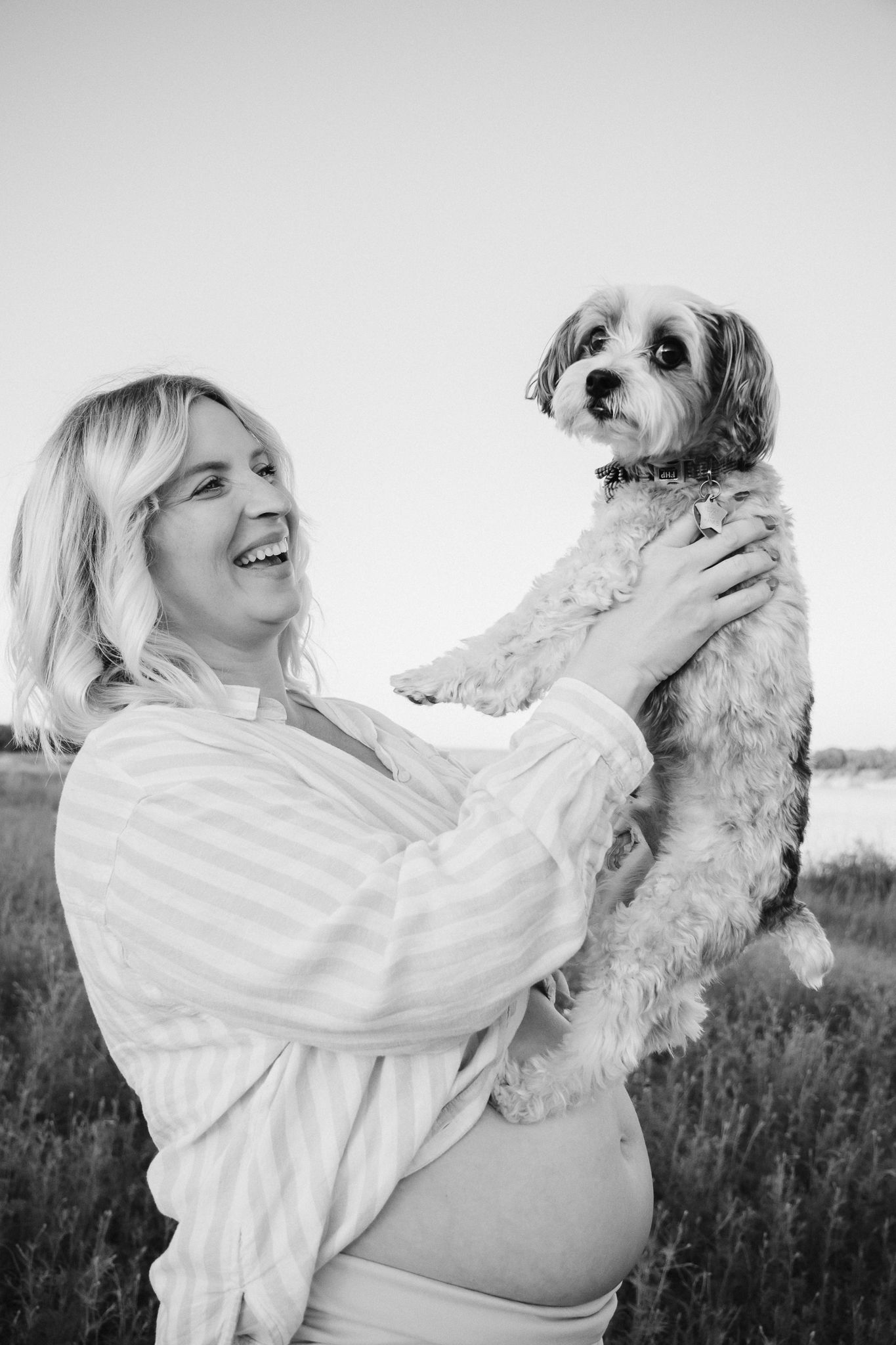 A series of four black and white photos showing joyful moments between a person and their small fluffy dog outdoors.