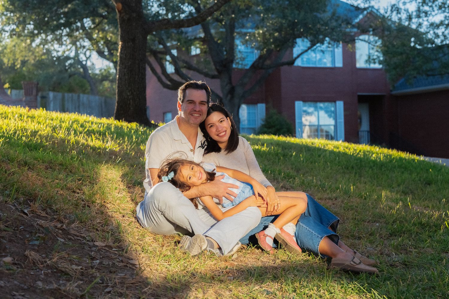 A couple lies together on a grassy hillside during golden hour sunlight.
