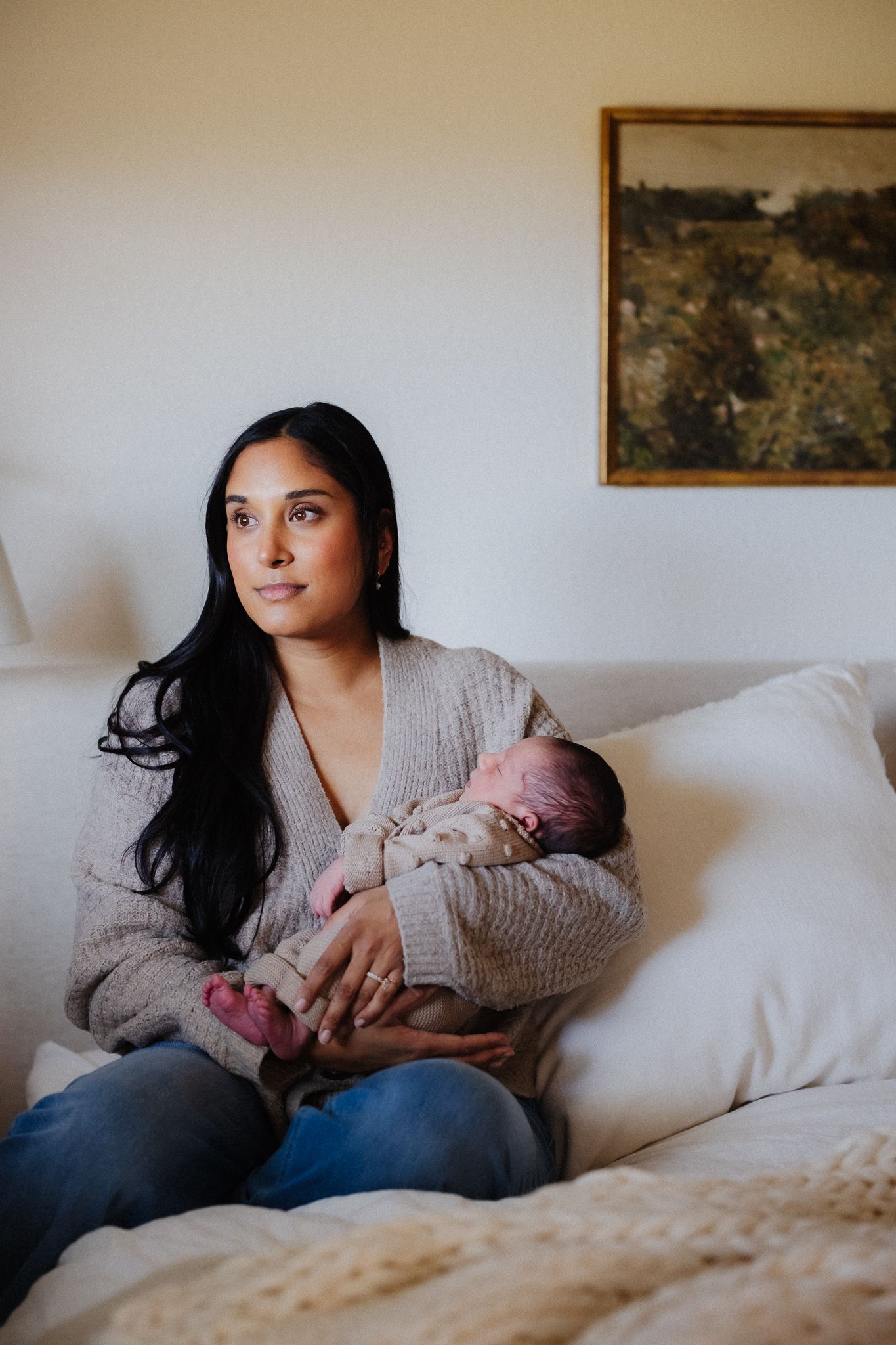 A mother and infant share a tender moment while resting together on a white couch.