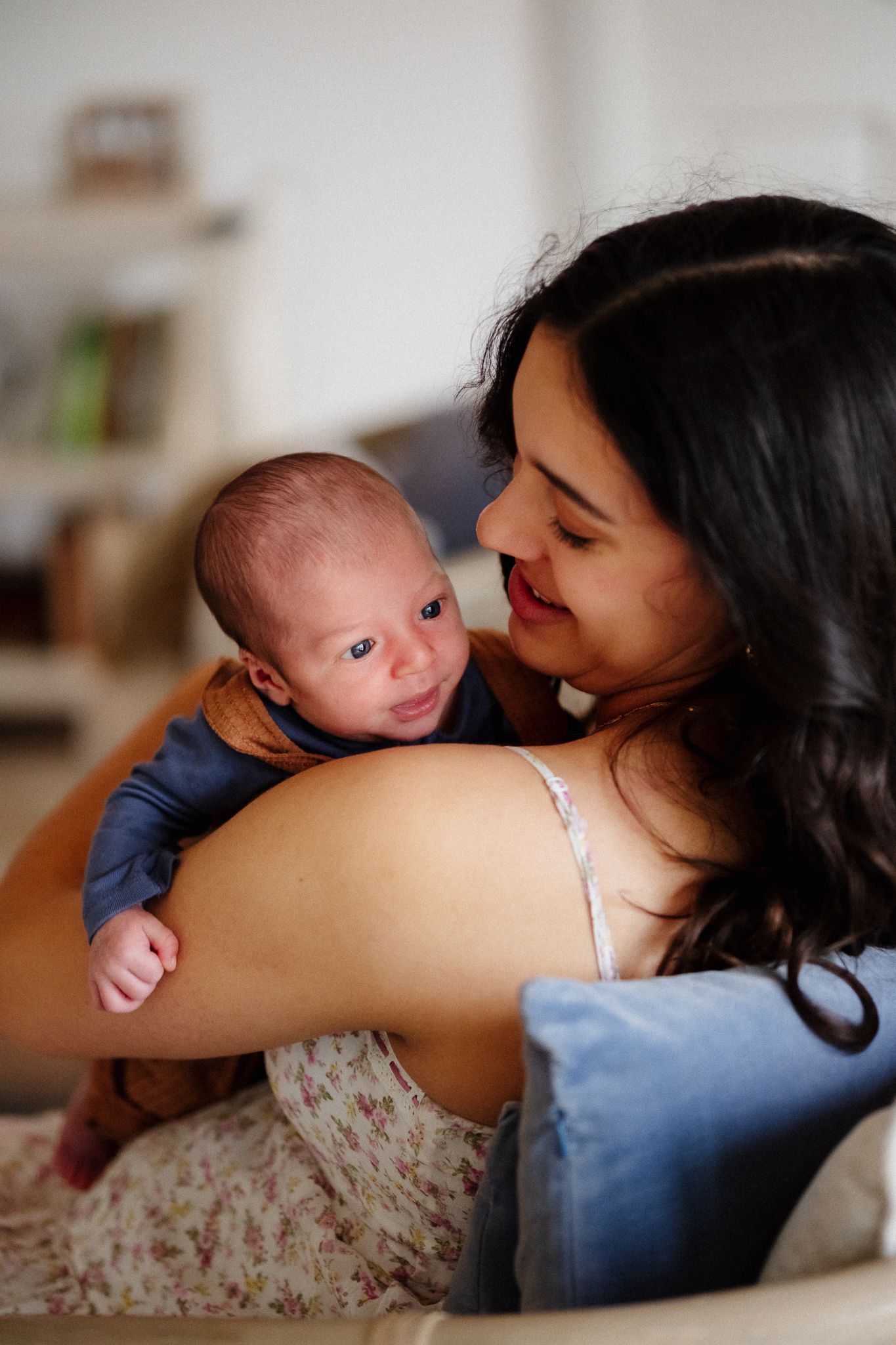 A tender moment between mother and newborn baby as they share a loving gaze while relaxing at home.