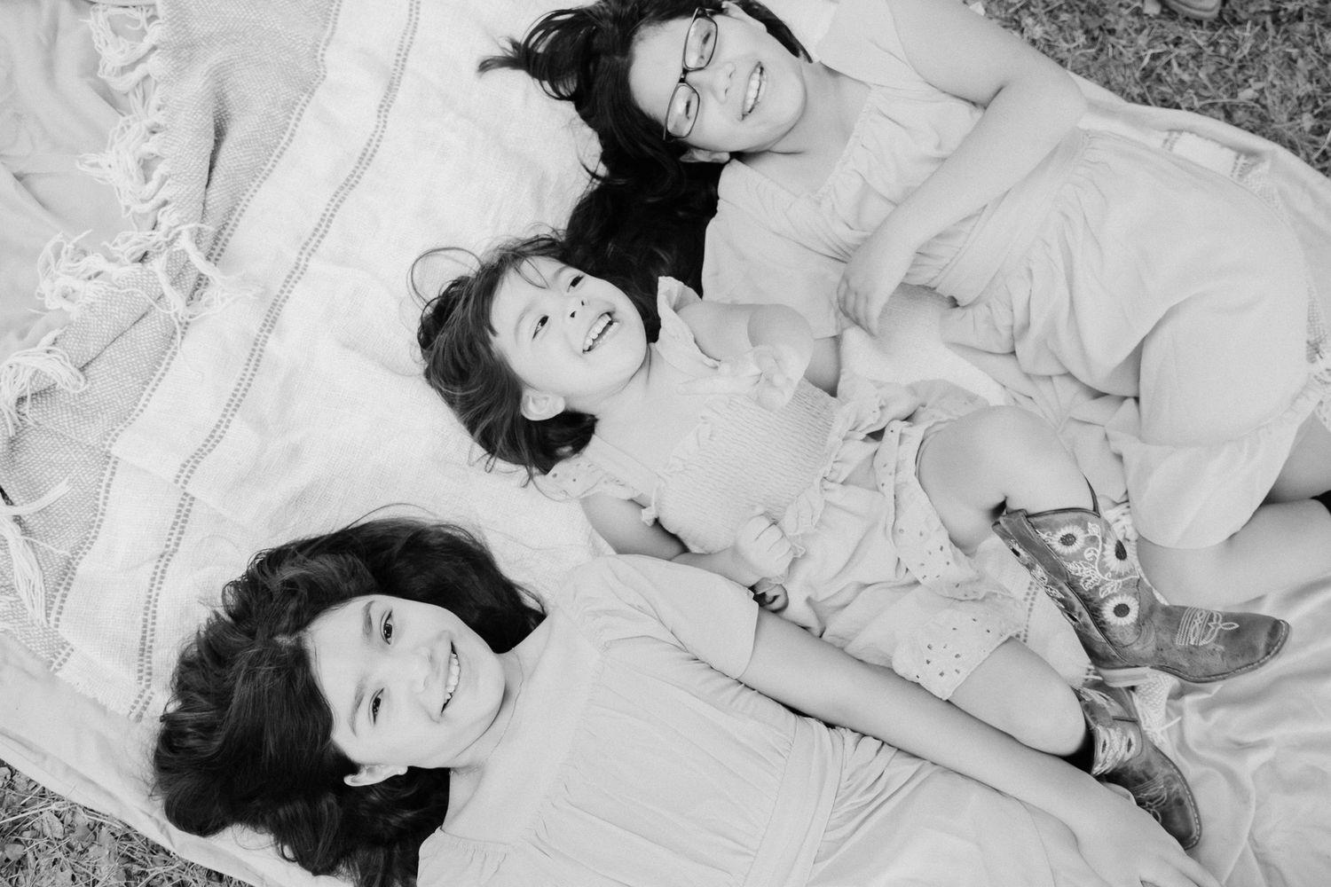 Black and white photo of three girls lying on a blanket outdoors, smiling and laughing together.