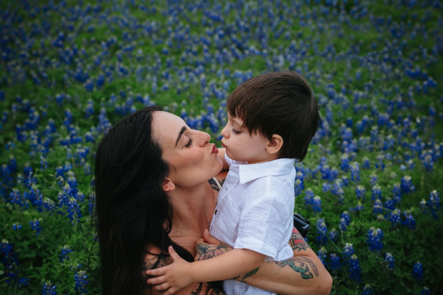 A mother and young boy share a sweet kiss in a vibrant Texas bluebonnet field.