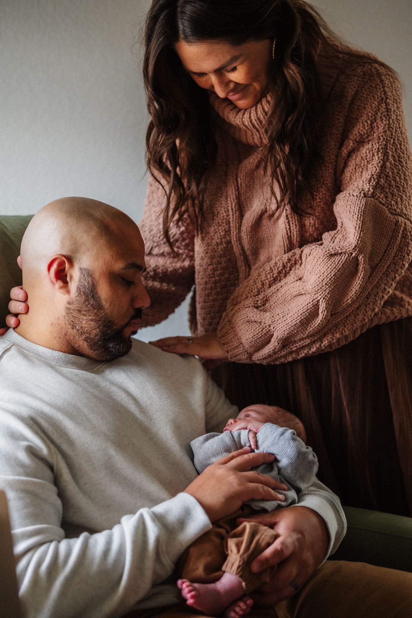 Intimate family portrait showing parents bonding with their newborn in warm, natural lighting.
