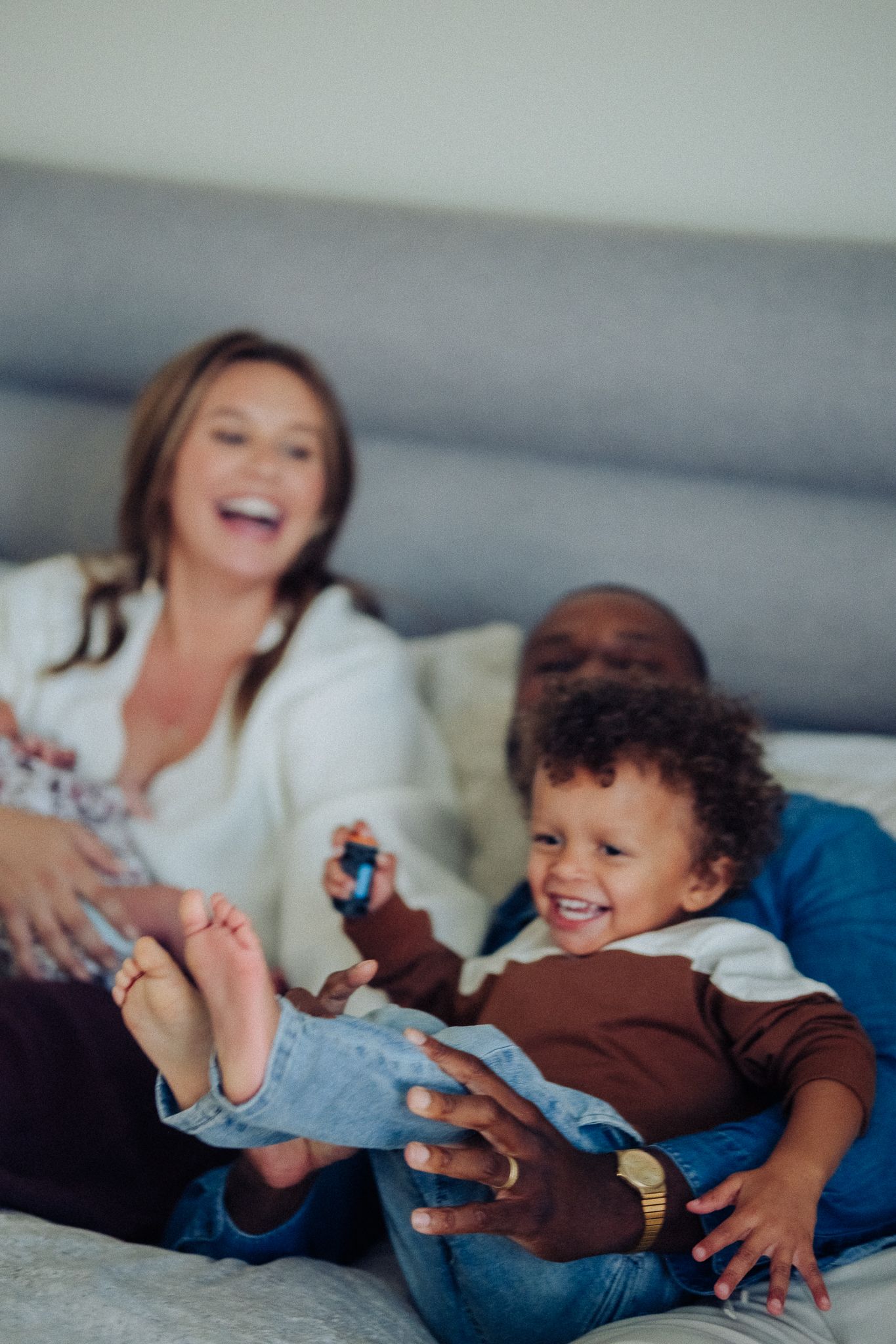 Happy mixed-race family with toddler laughing and playing together on a bed at home.