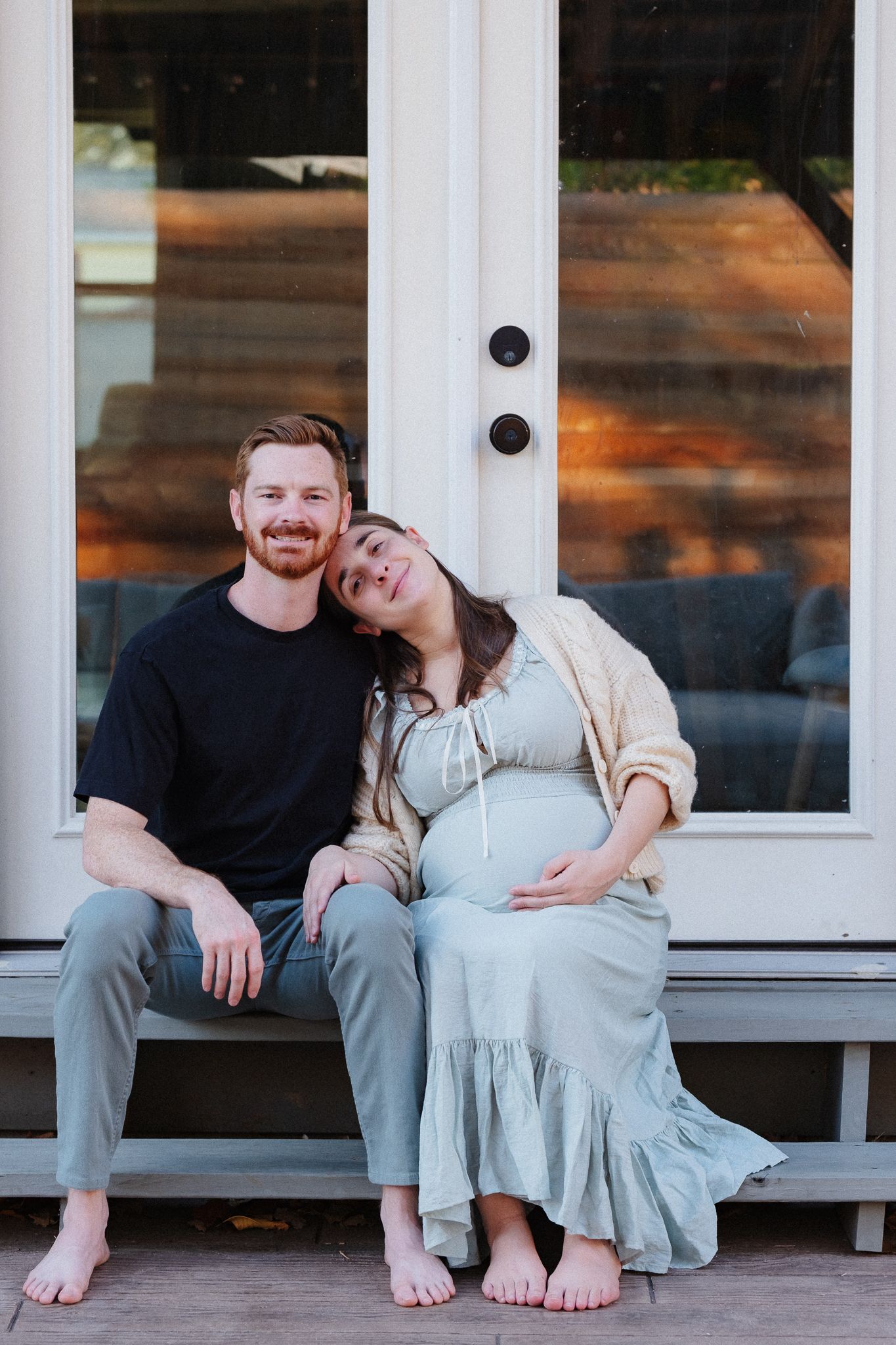 Casual maternity portraits of couple relaxing on white porch bench.