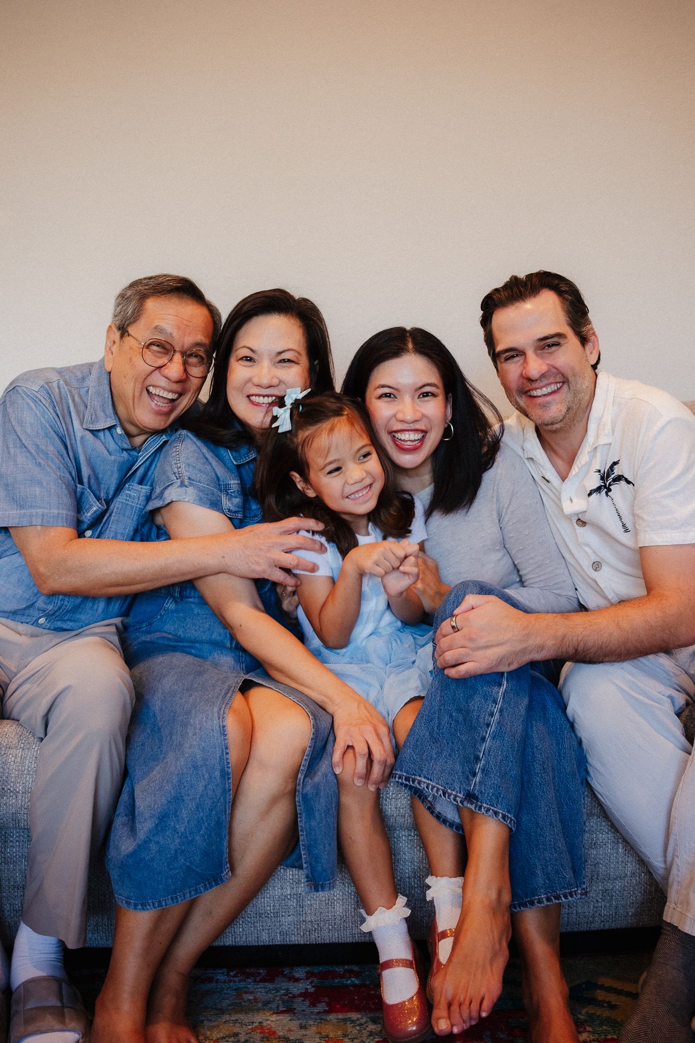 Multi-generational family wearing denim sitting close together on couch for casual portrait session.