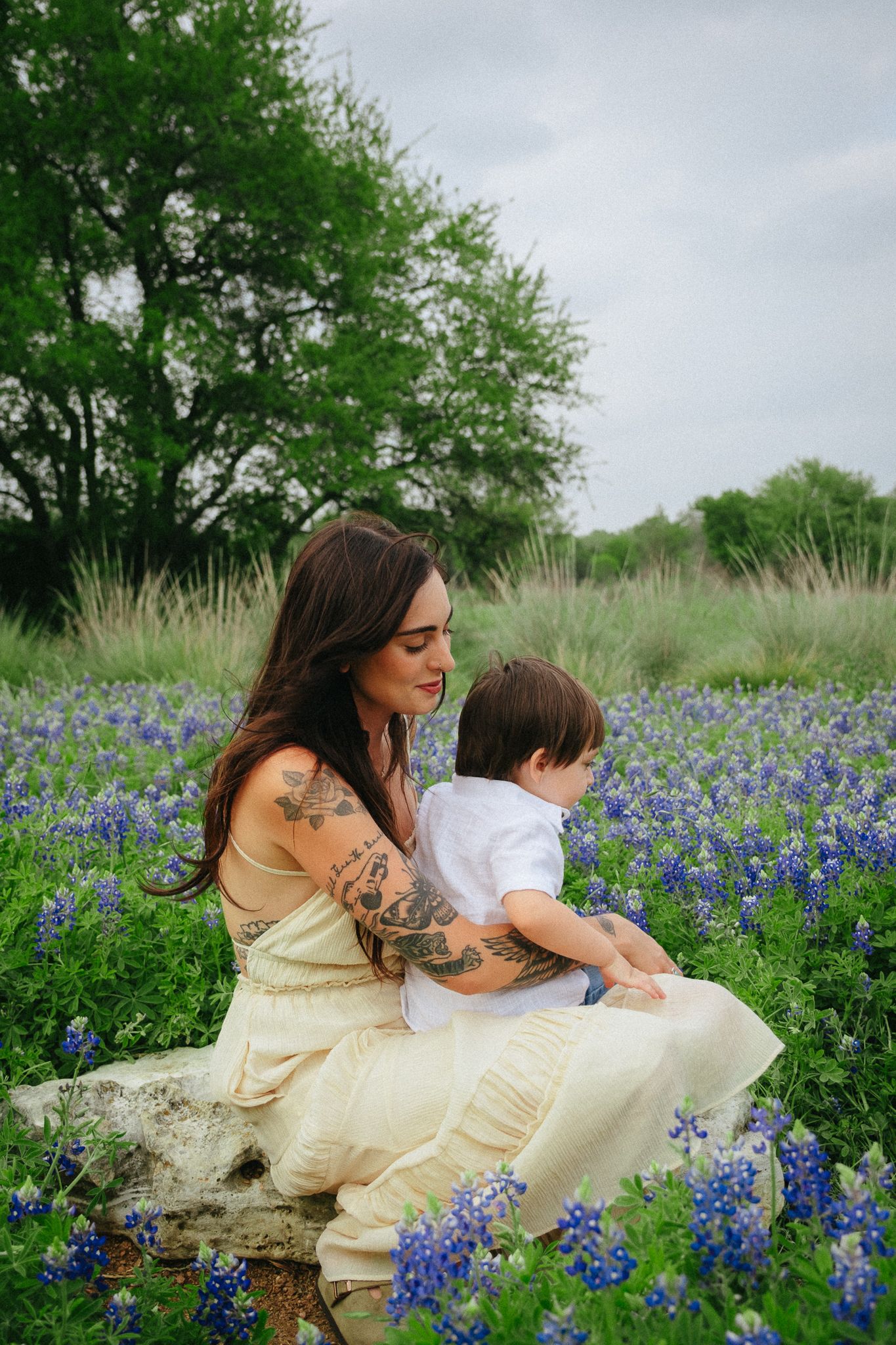 A mother and child sit together in a field of vibrant blue wildflowers on a spring day.
