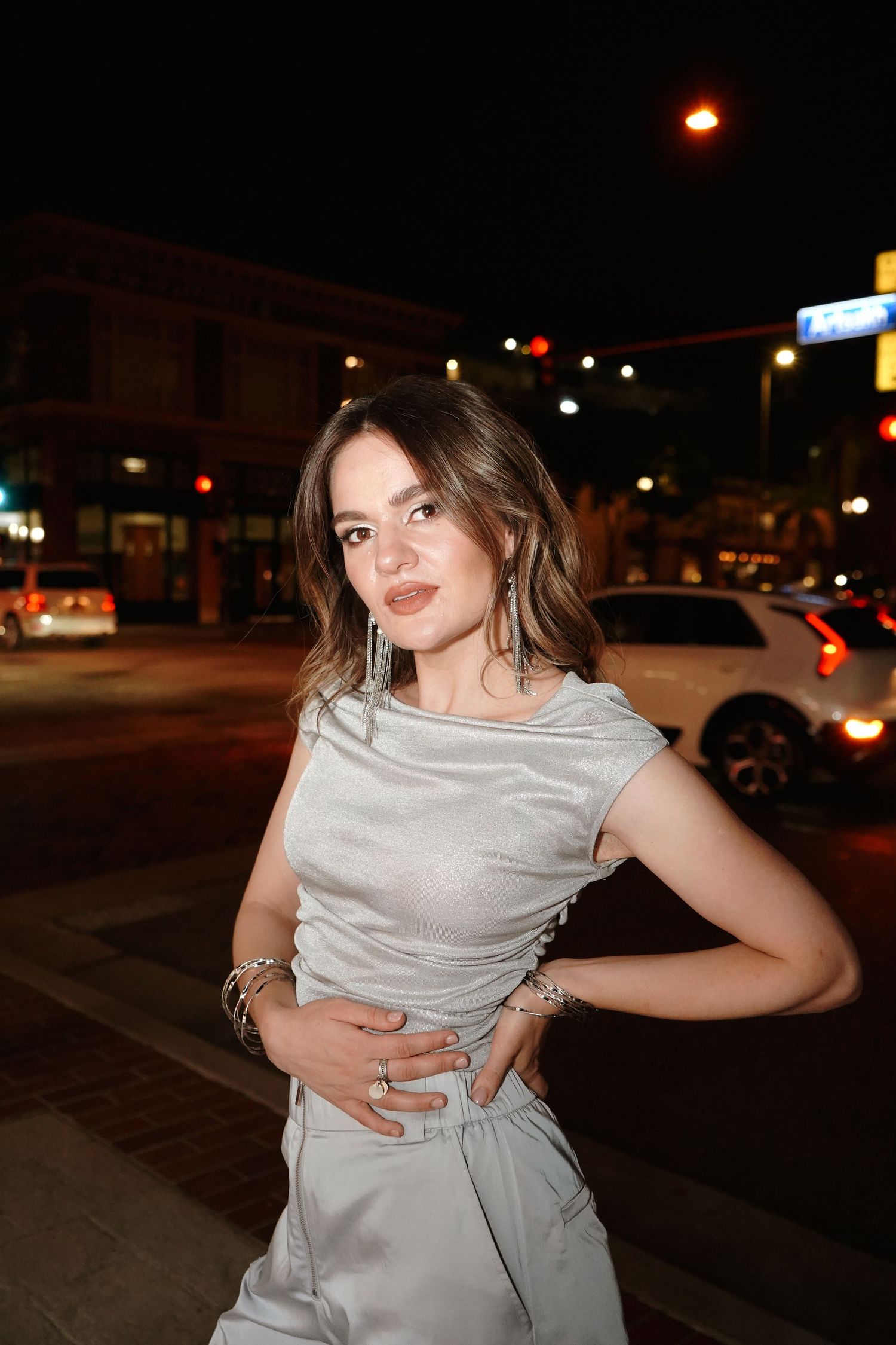 Nighttime street scene with someone posing in a light gray dress against an urban background with glowing lights.