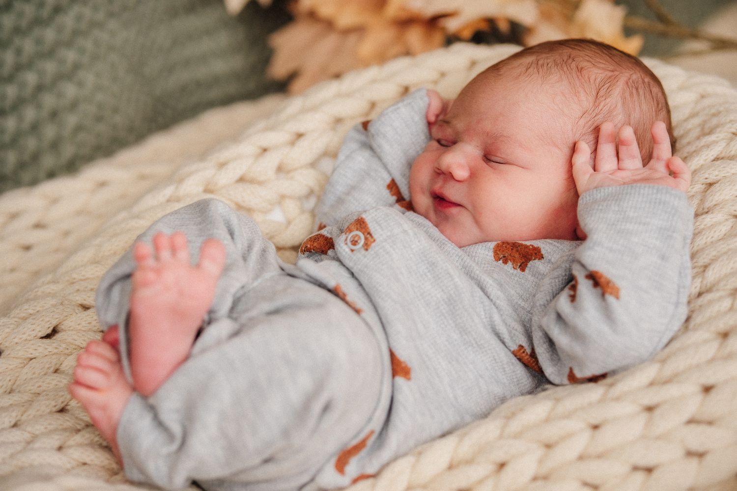Newborn baby sleeping peacefully in soft gray clothing on a textured white blanket.