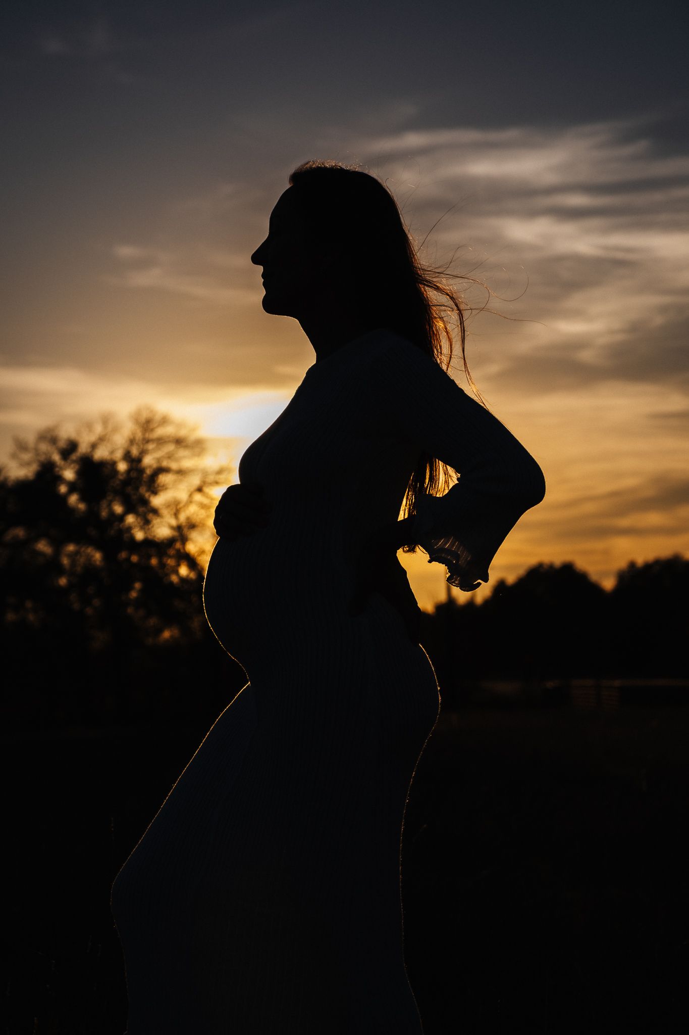 A dramatic silhouette of an expectant mother against a dusky sunset sky.