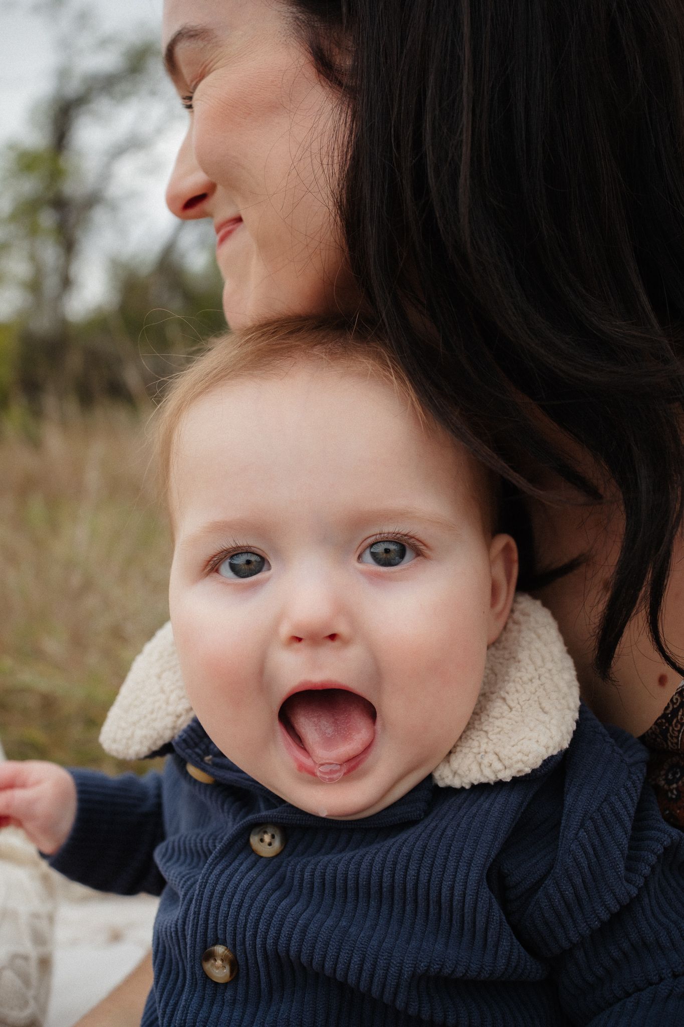 Close-up of a smiling baby wearing a navy blue knit sweater with buttons.