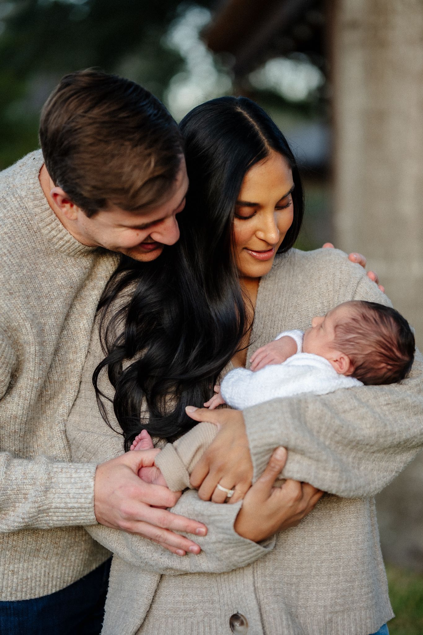 Intimate moment with newborn baby being held and cradled in beige sweater.