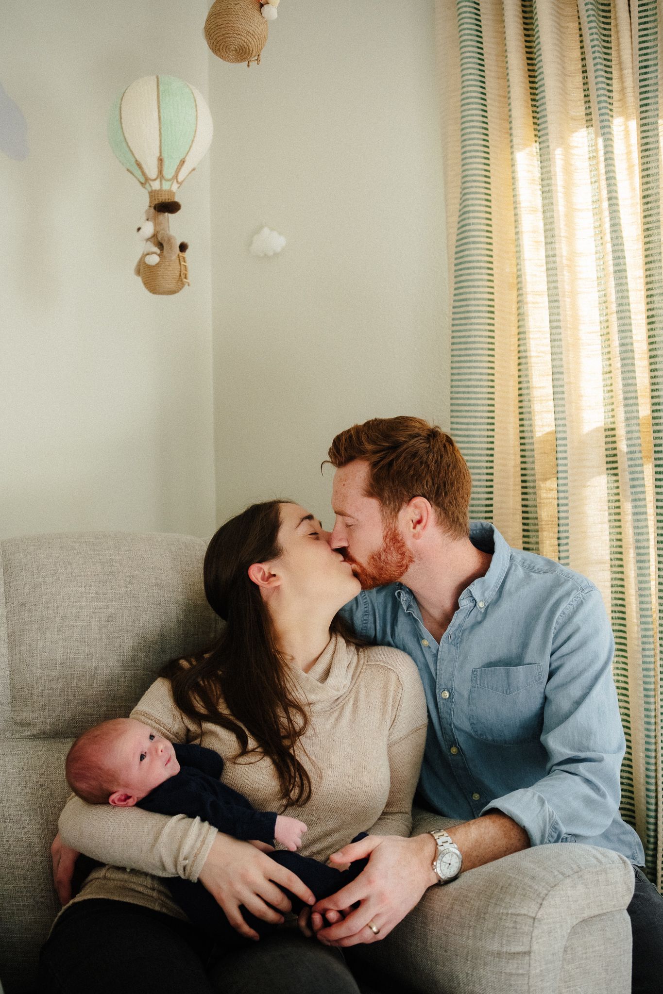 A family shares intimate moments of love and bonding with their newborn baby while sitting together on a couch.