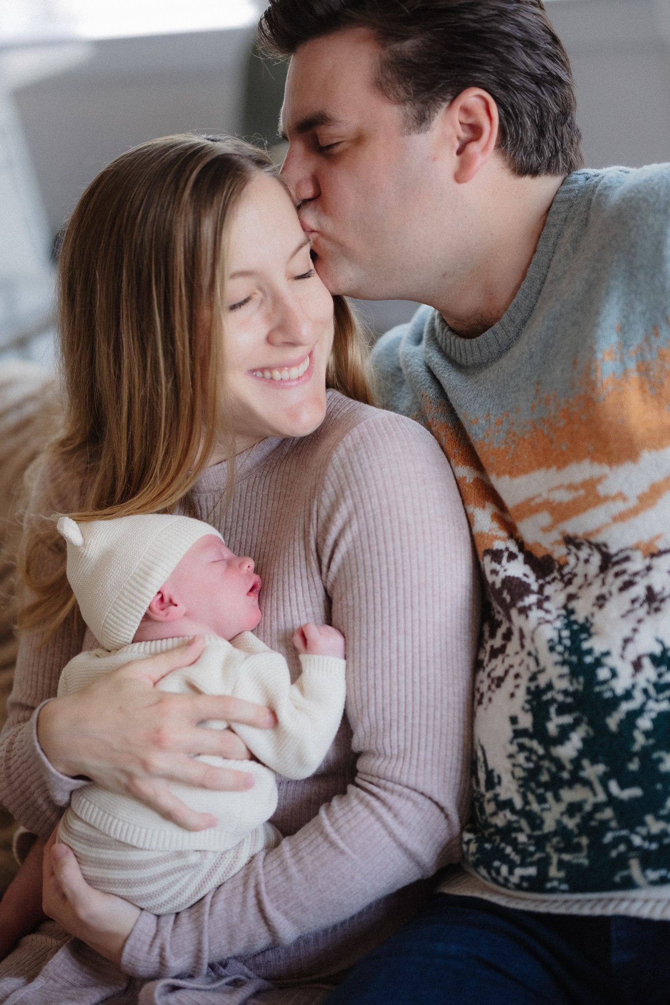 A tender family moment as parents share a loving embrace while holding their newborn baby in a cozy indoor setting.