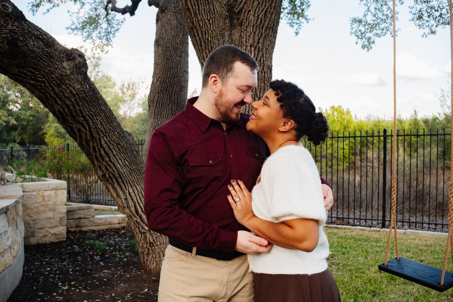 Candid family moments captured under a large tree with a swing in a fenced backyard.