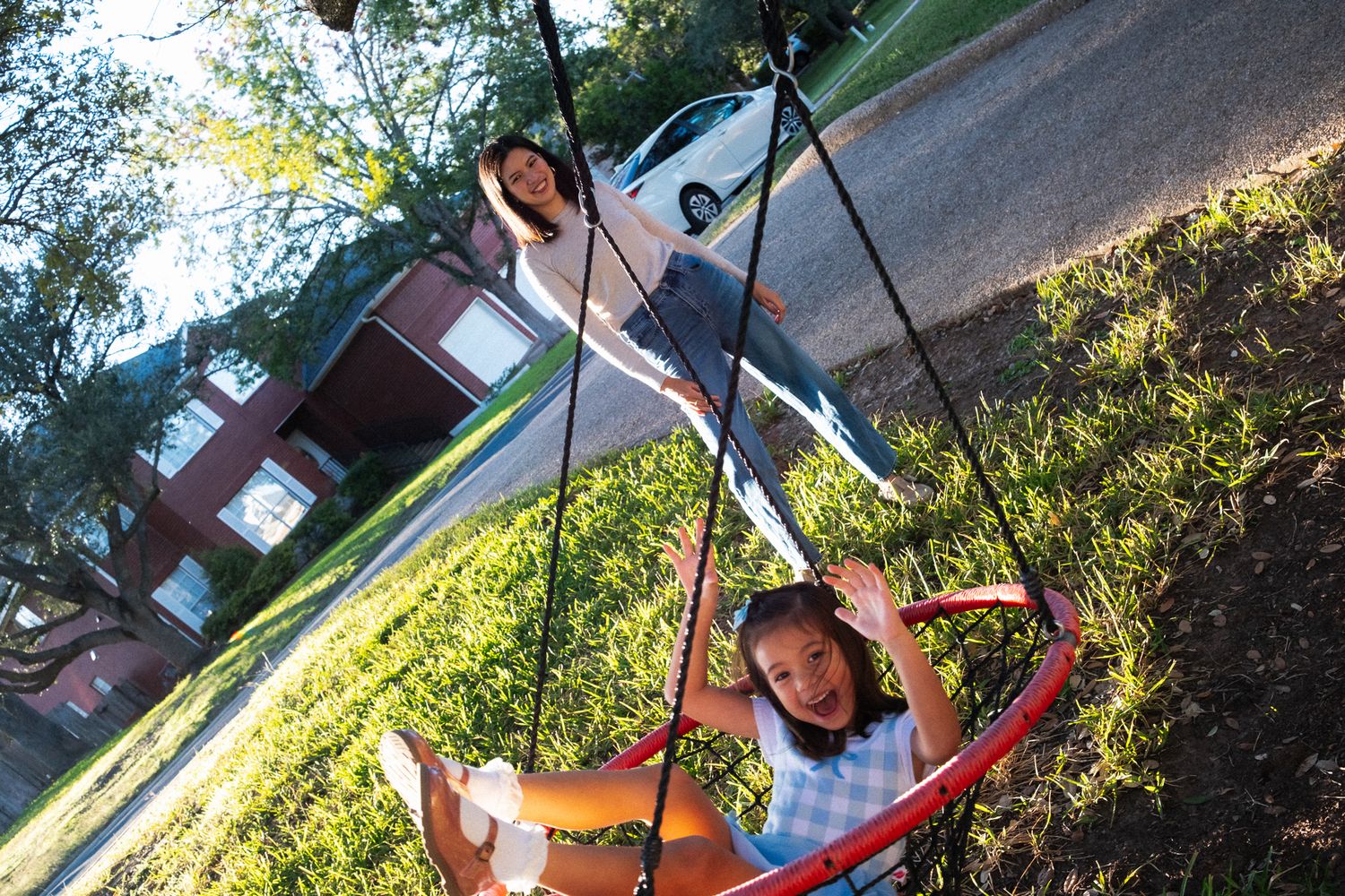 A person swinging on a backyard tree swing during a sunny afternoon with green foliage in the background.