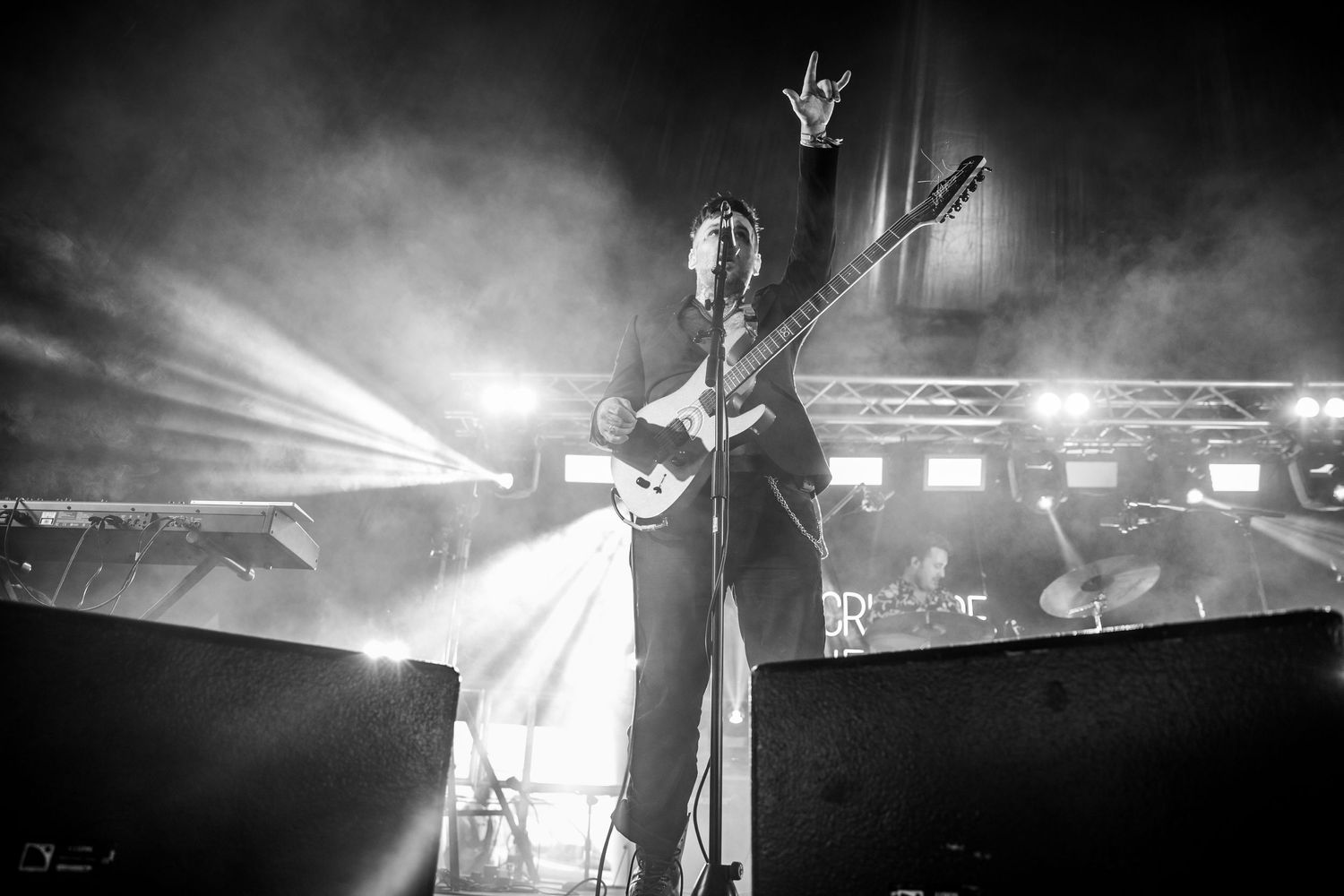 A dramatic black and white concert photo of a guitarist performing on stage with bright spotlights and fog effects.