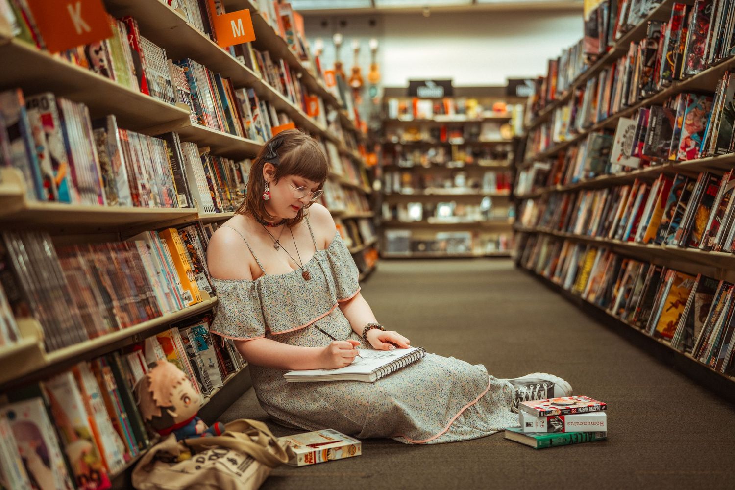 Young reader engages with books while sitting on the floor of a library aisle surrounded by bookshelves.