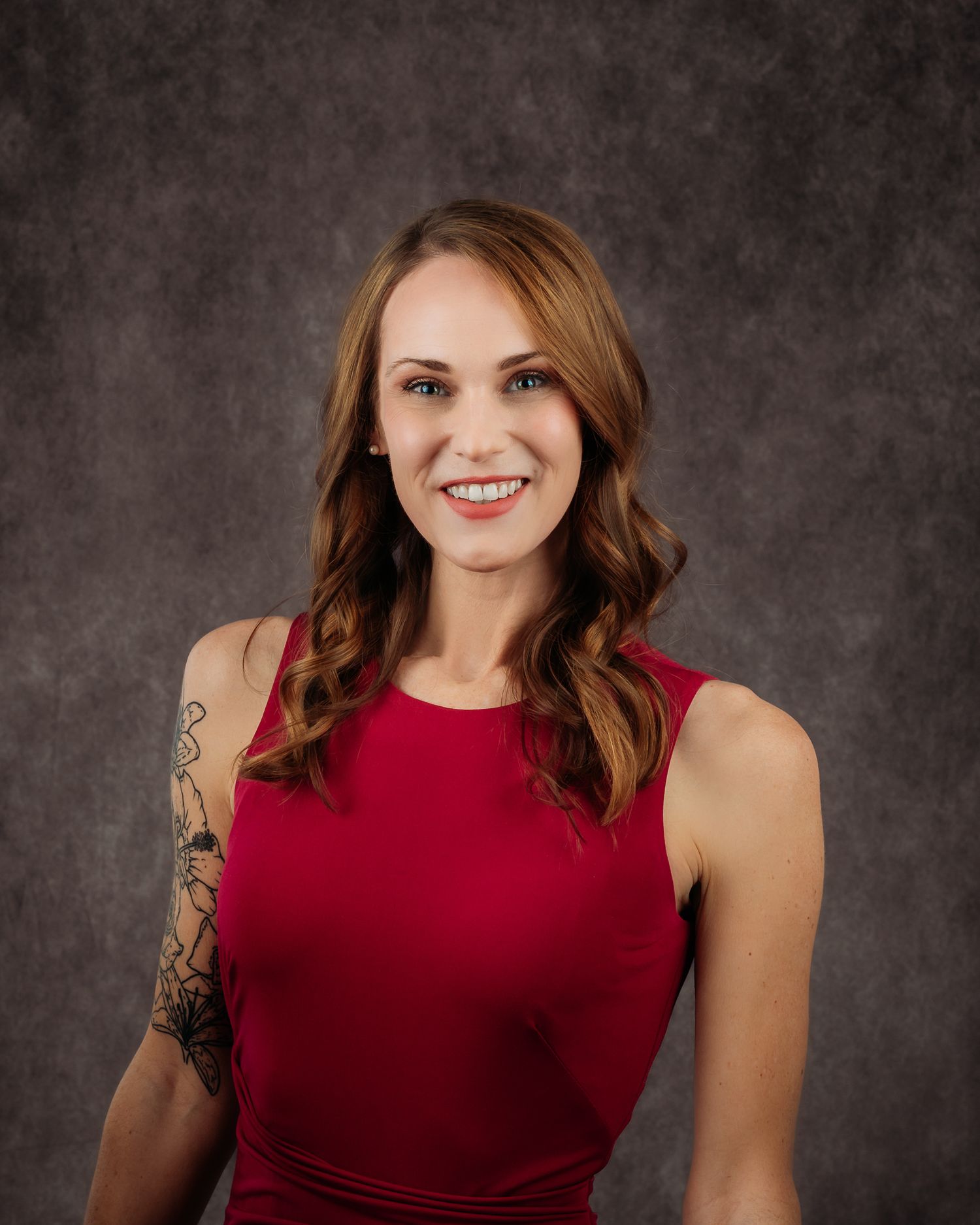 Professional studio portrait against dark gray background featuring someone in a sleeveless burgundy dress.