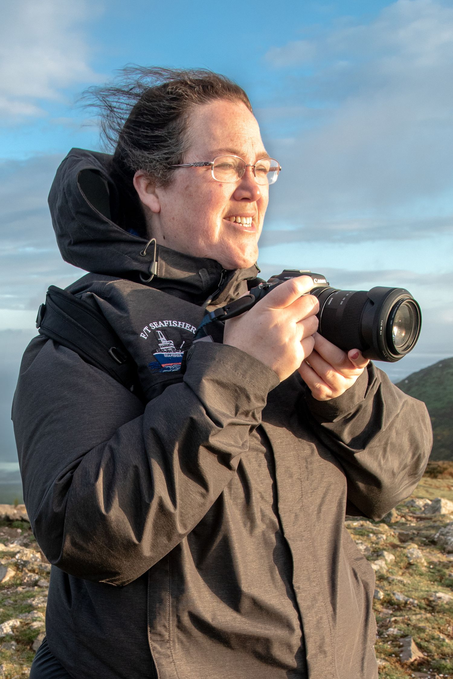 Photographer atop a hillside with windswept hair.