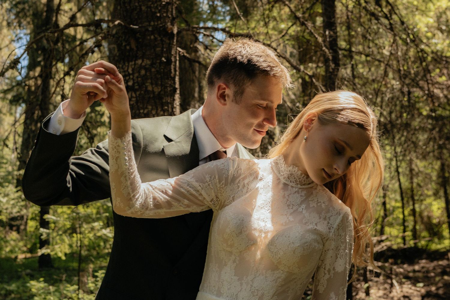 Couple dances together in sunlit forest wearing wedding attire on their special day.