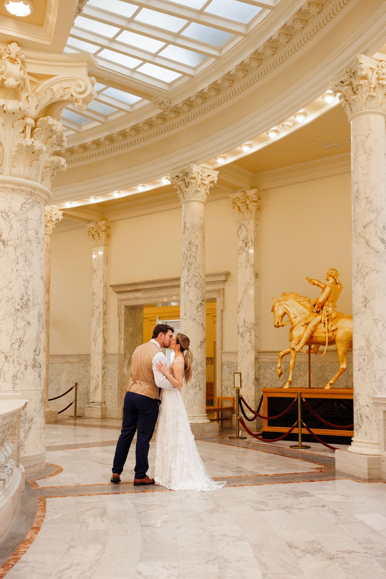 Elegant architectural interior with marble columns and a golden equestrian statue in museum or palace setting.