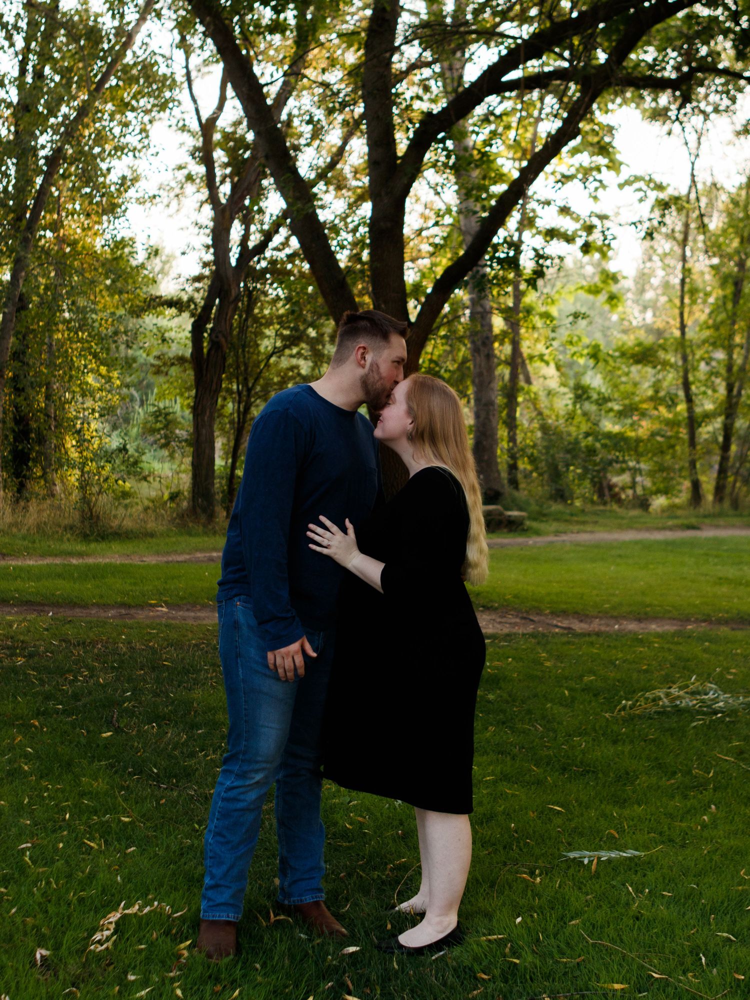 A romantic outdoor photo session in a sunlit park with autumn trees in the background.