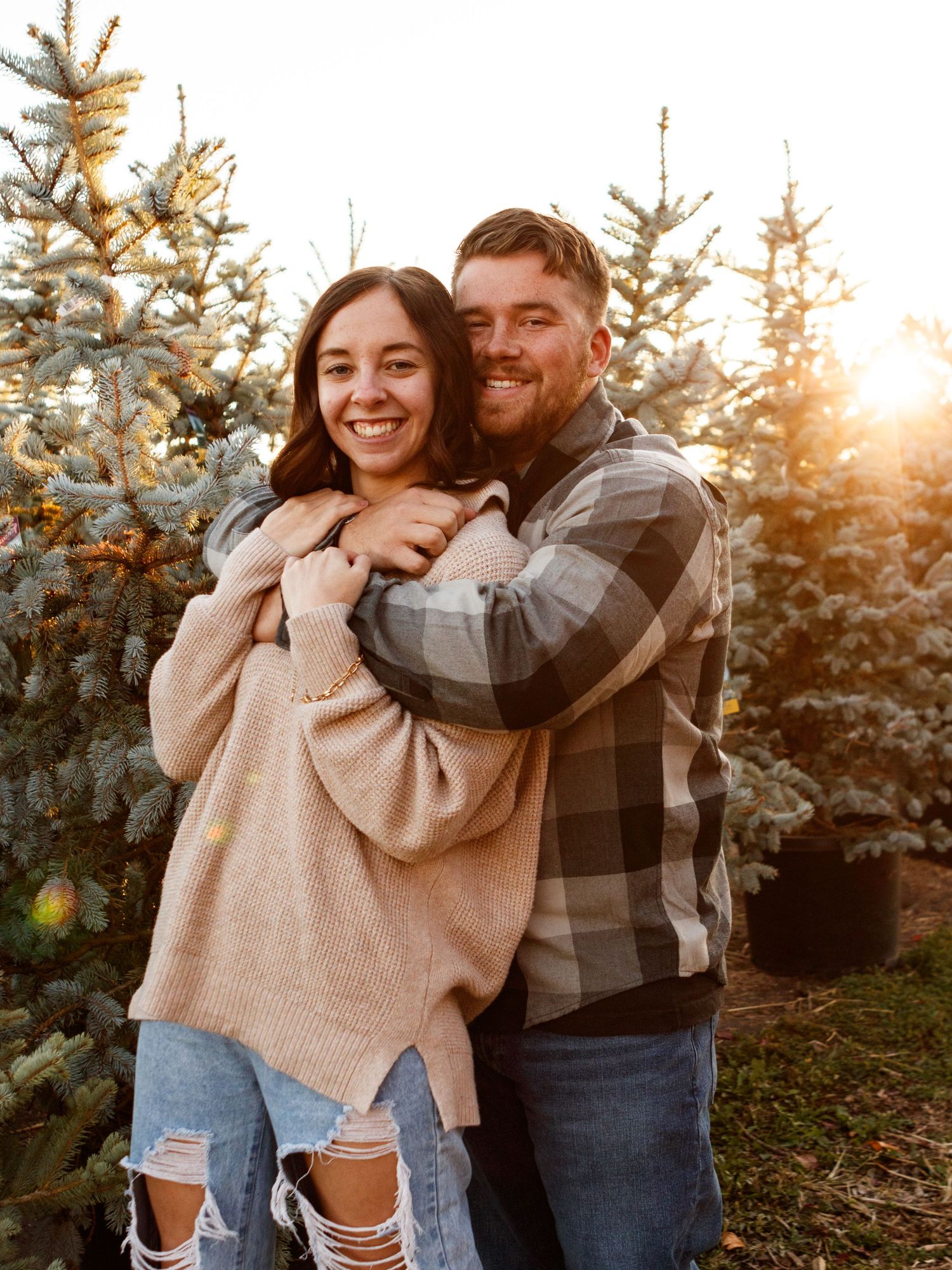 Couple hugging eachother with christmas trees in the background.