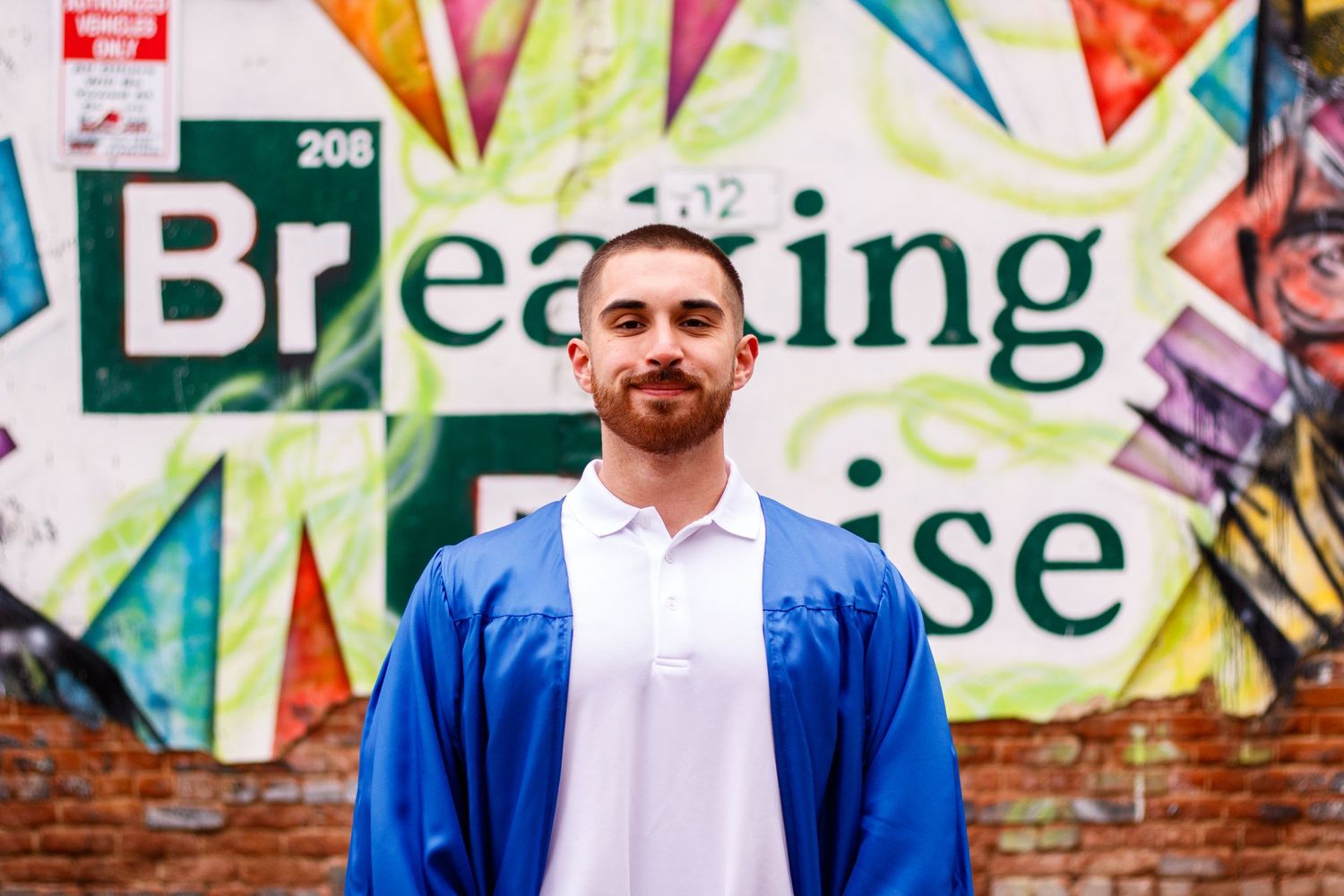 A person in a blue jacket and white polo stands in front of a colorful graffiti wall with text.