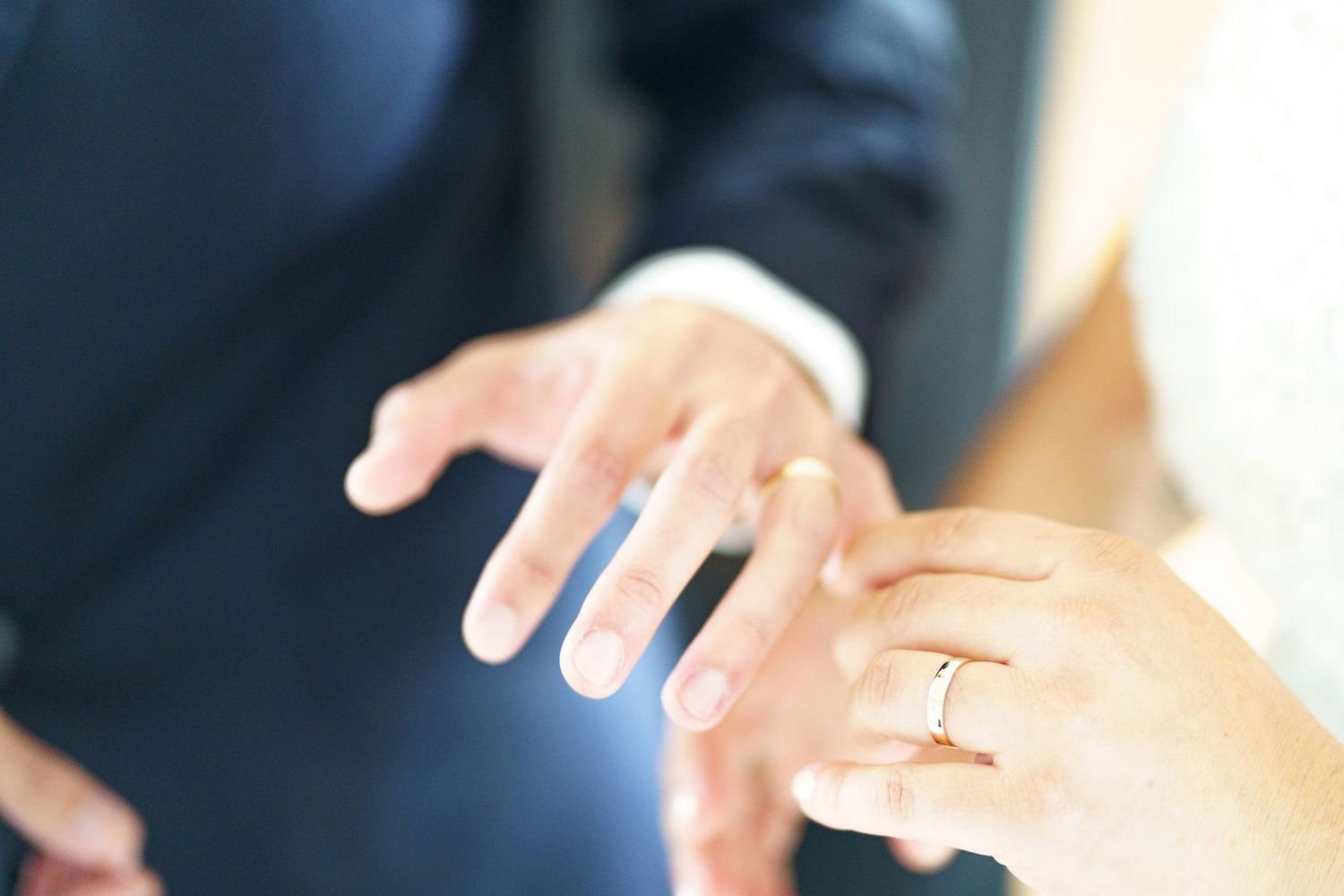 Close-up of bride placing a gold wedding ring on grooms finger during the wedding ceremony.