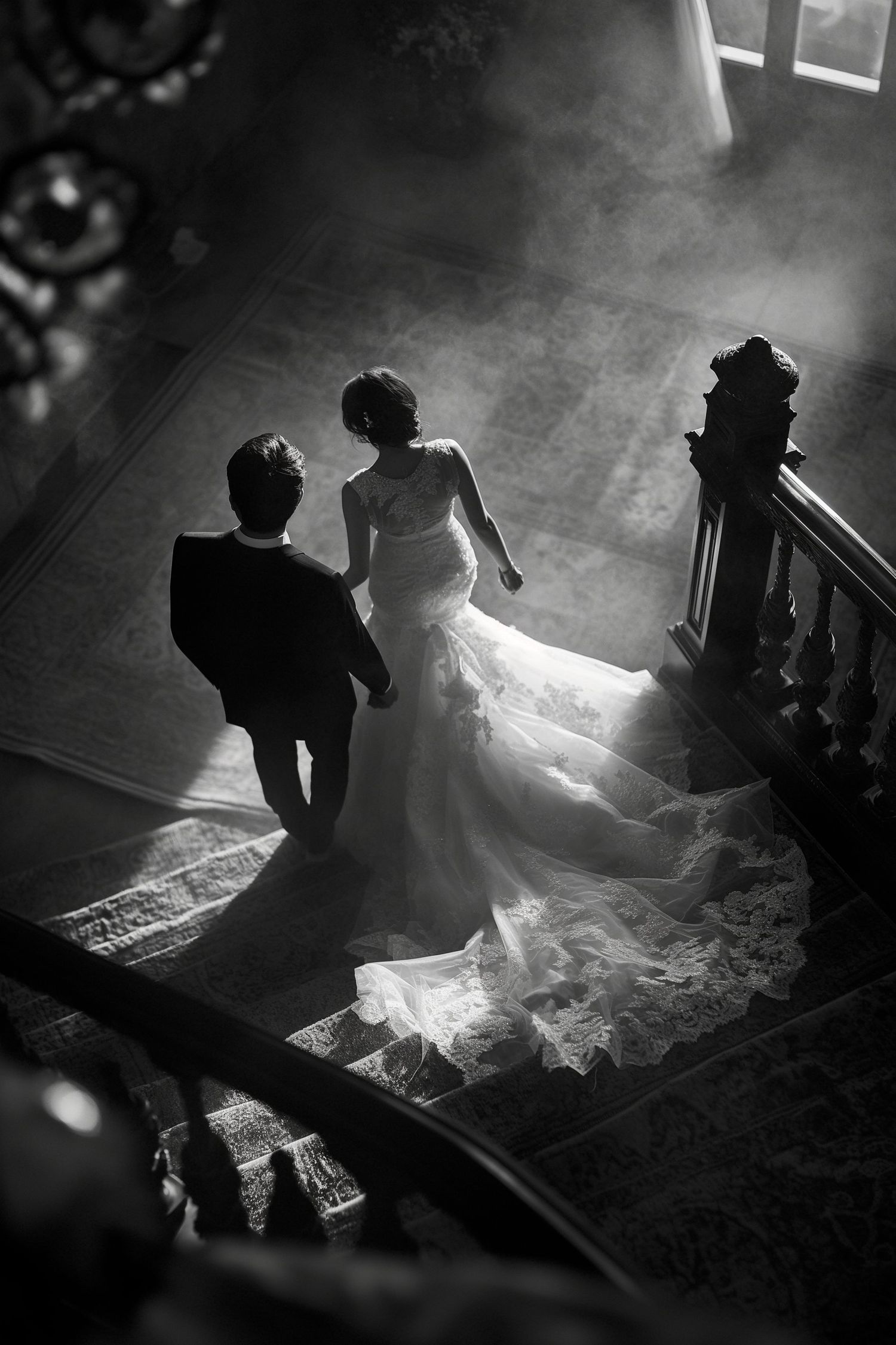 Dramatic black and white aerial view of bride and groom ascending a grand staircase in misty light.