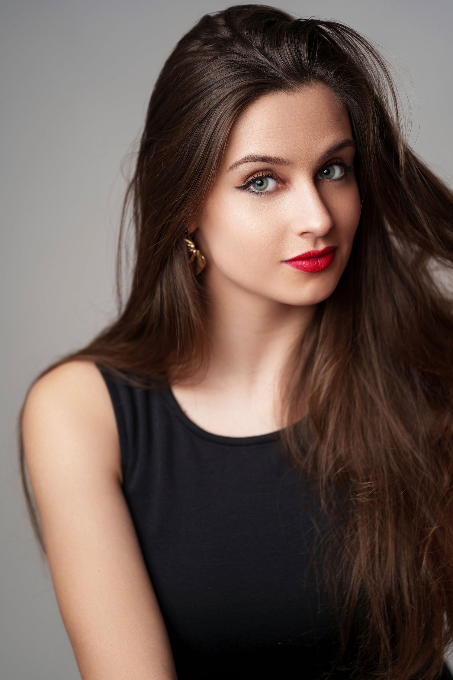 Brunette woman with long hair, blue eyes and red lips in black dress portrait.