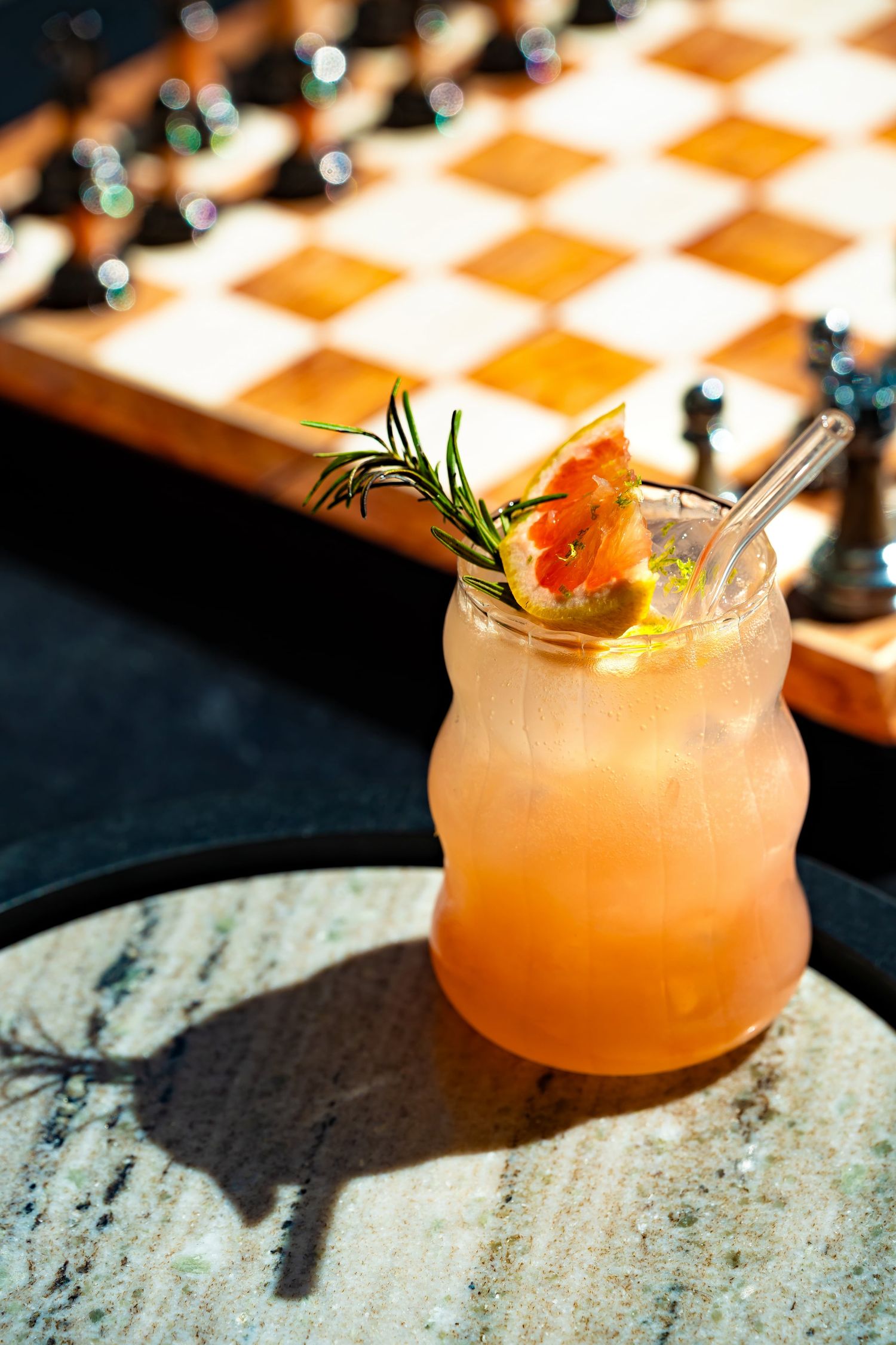 Refreshing grapefruit cocktail with rosemary garnish in mason jar near chess board outdoors.