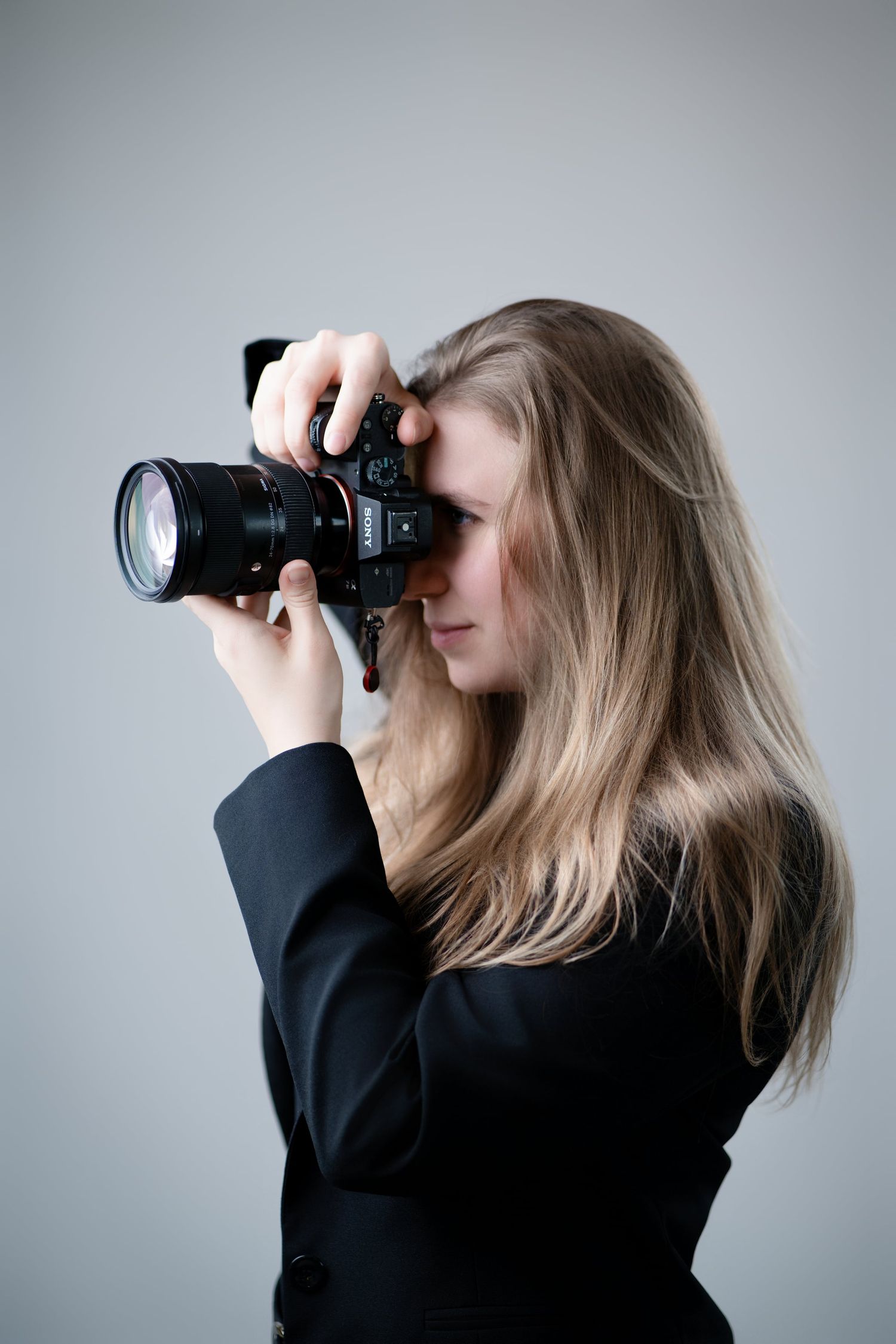 Blonde woman in black blazer photographing with professional DSLR camera in studio.