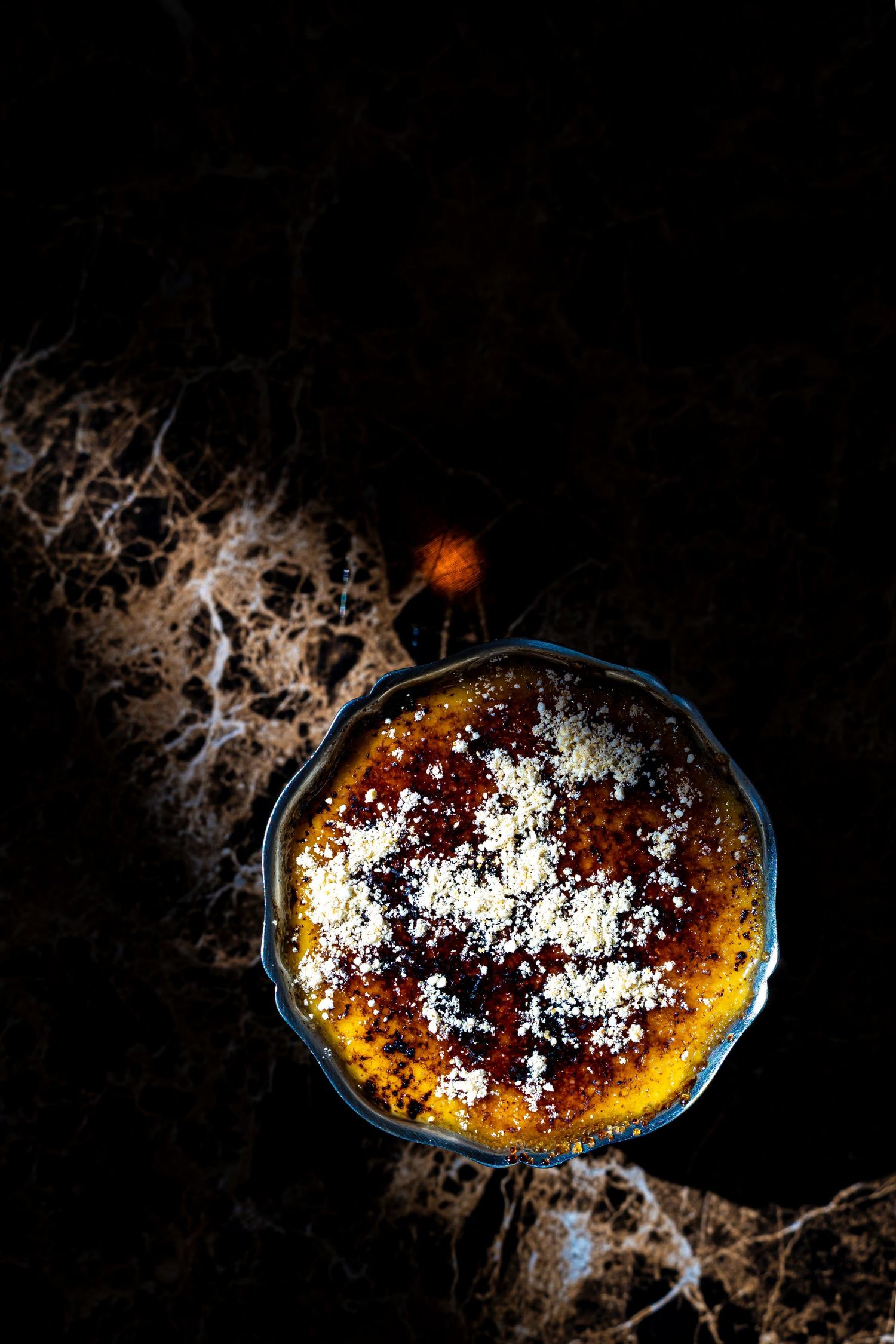 Top view of golden creme brulee with caramelized sugar crust in vintage dish on dark marble.