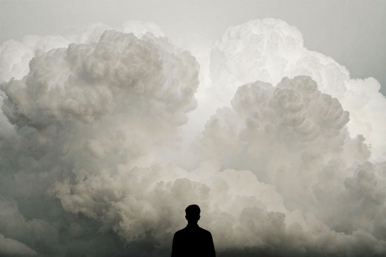 A solitary silhouette stands before massive billowing storm clouds in a dramatic monochrome scene.