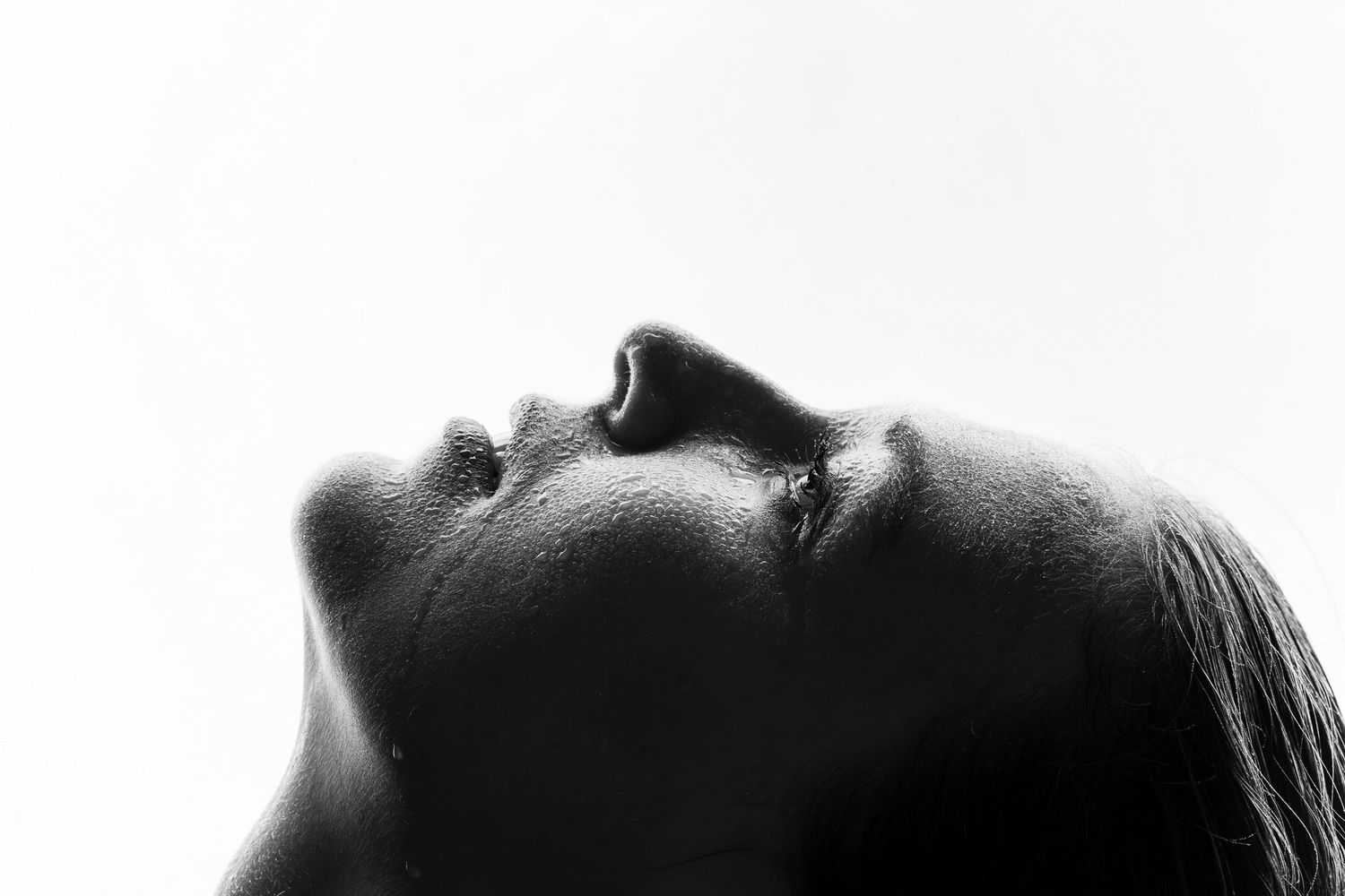 Black and white close-up profile of a woman with head tilted back against a white background.