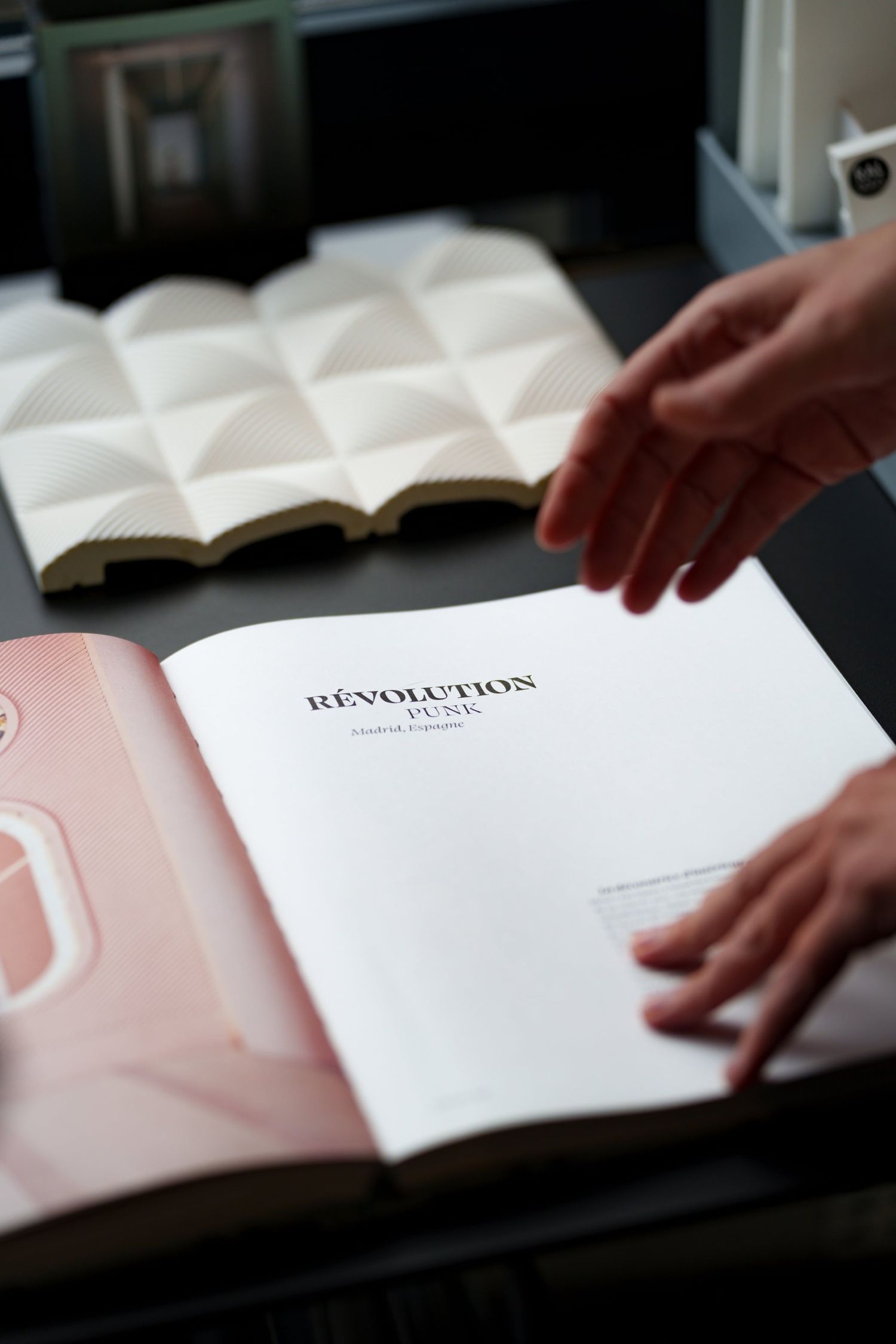 Hands opening a book titled Revolution Pure on a dark surface with design samples nearby.