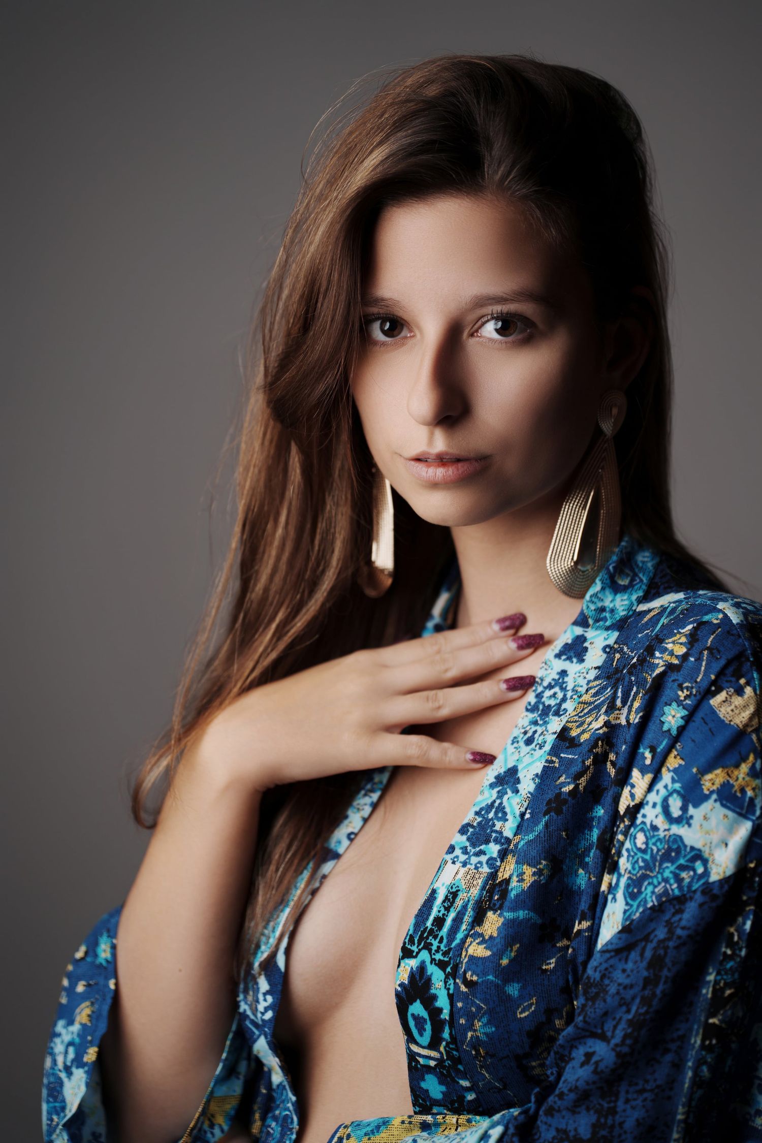 Young woman in blue floral robe with gold drop earrings posing in studio.