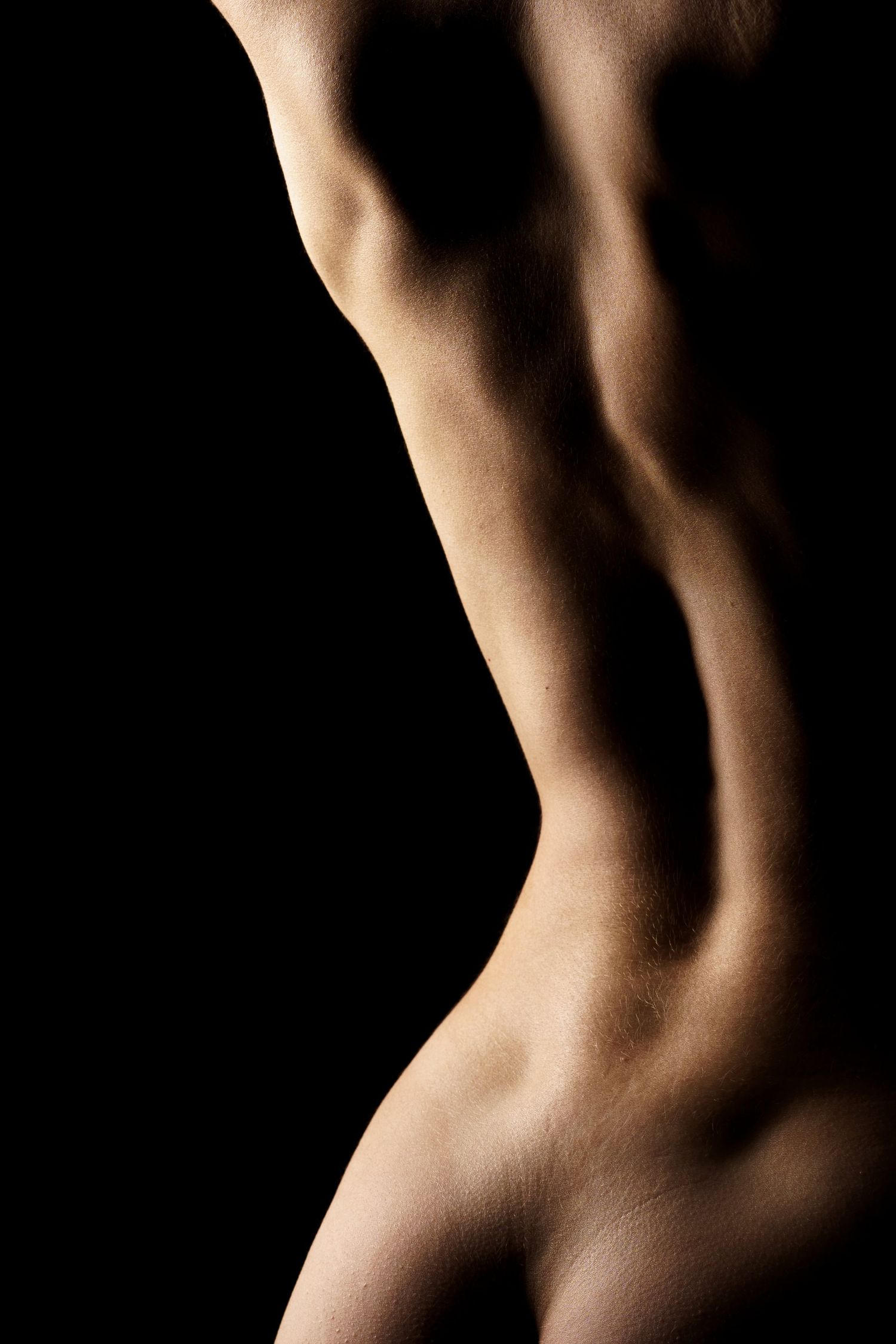 Artistic black and white close-up of a womans bare back and torso against a dark studio background.