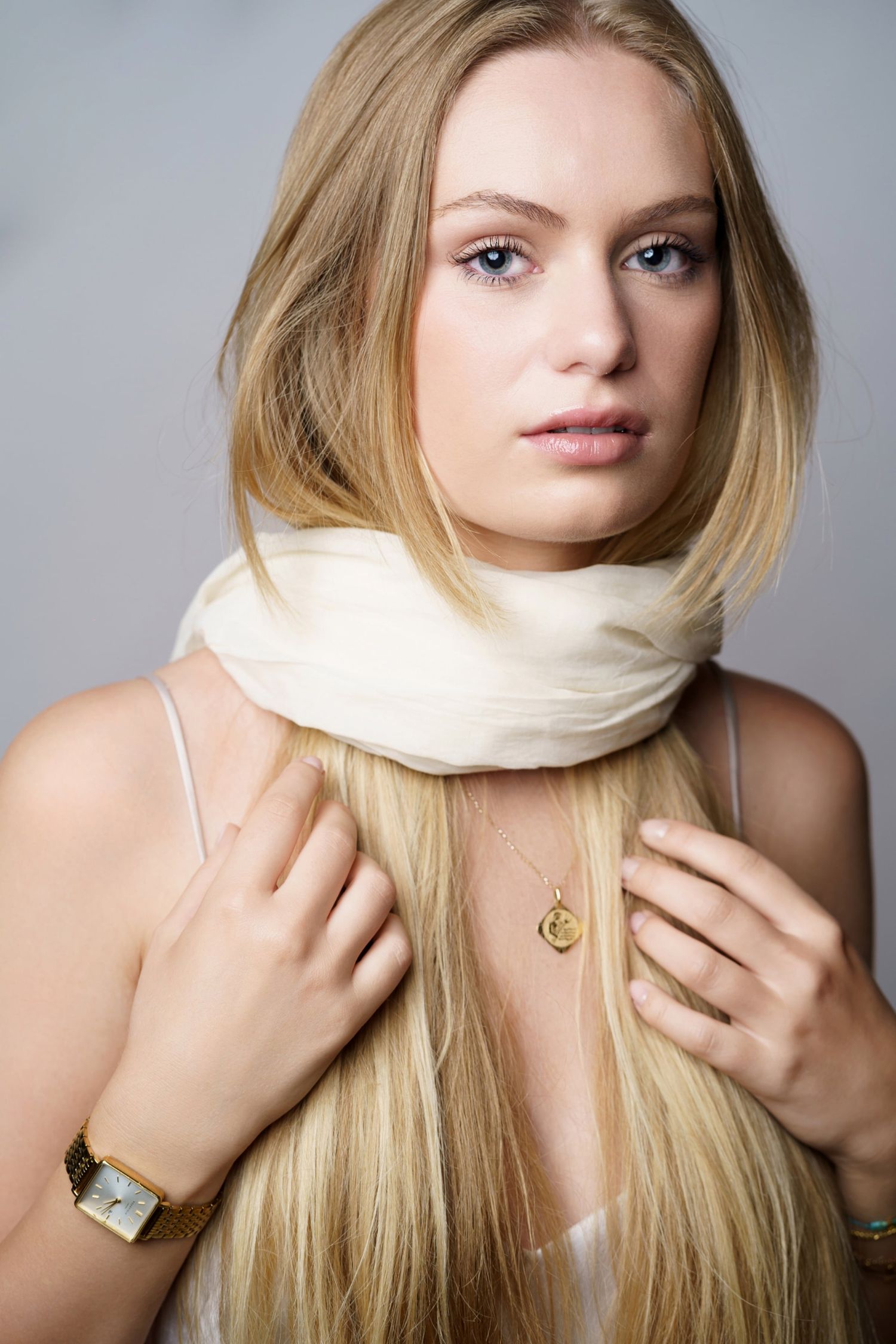 Blonde woman wearing white scarf and gold necklace with watch poses for portrait photo.